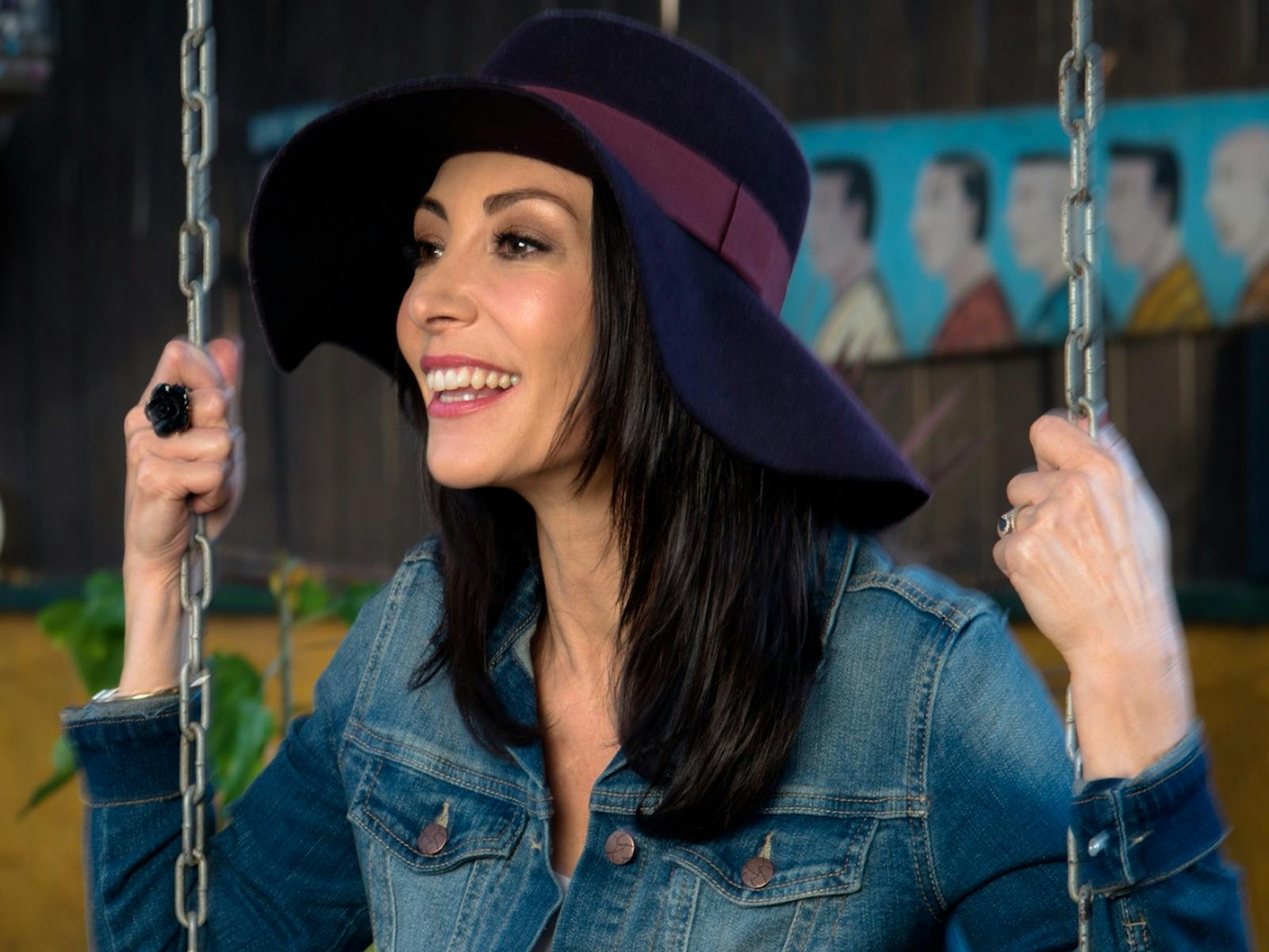 colour photo of Danielle De Andrea on a swing wearing denim jacket and hat