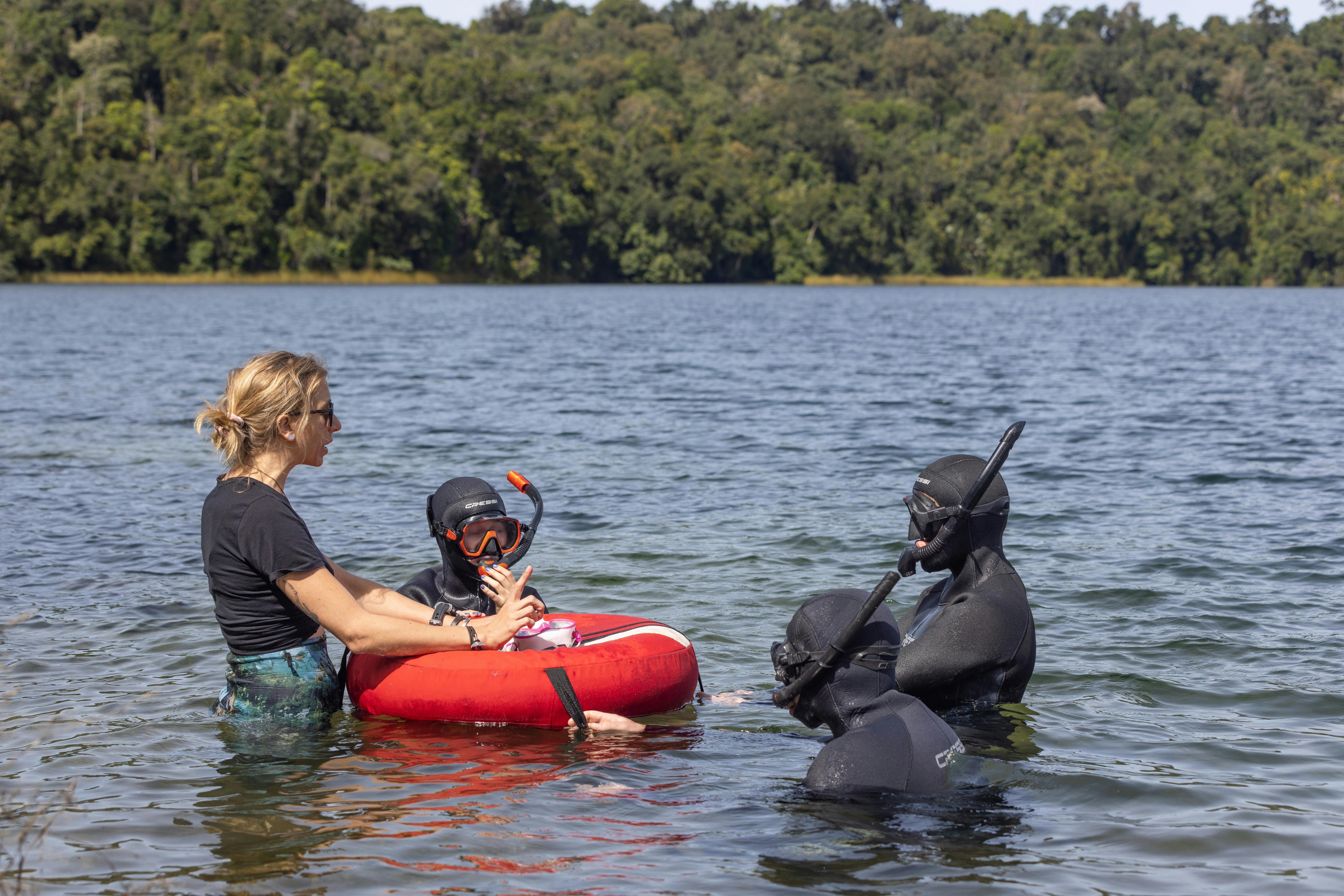 Instructor is standing with 3 students teaching them freediving skills in the shallow water