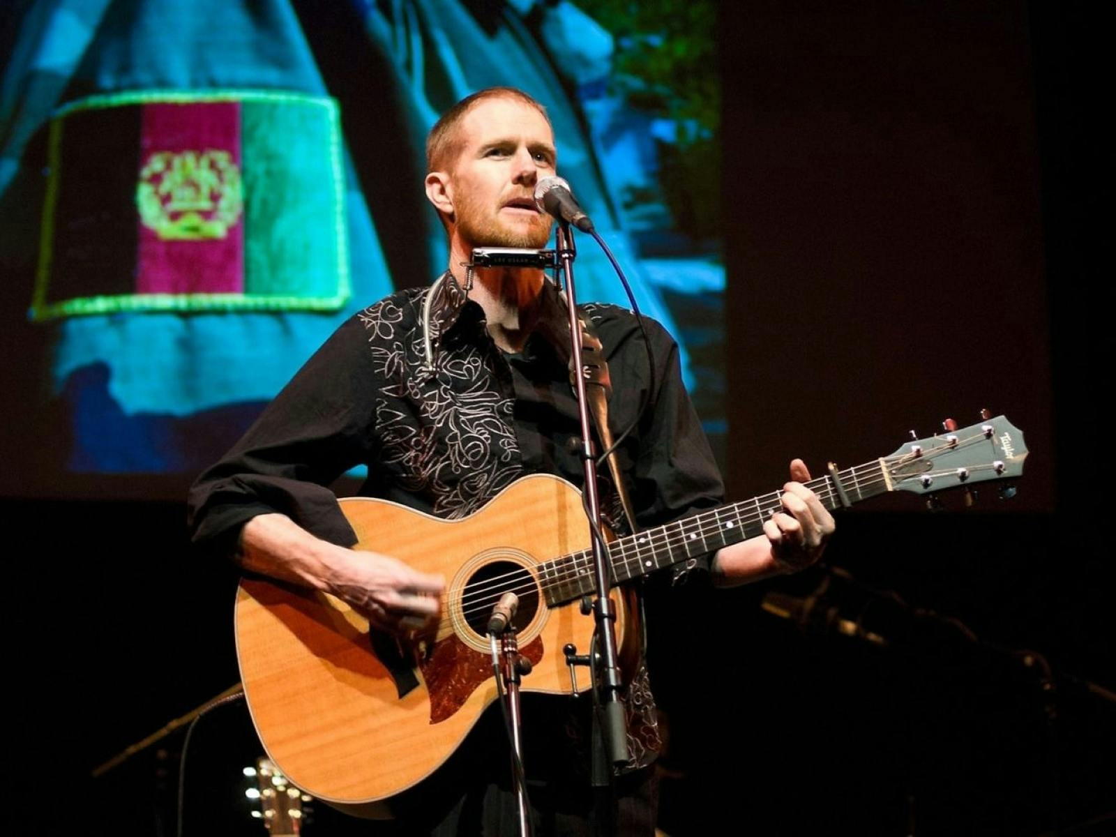 musician Fred Smith performing on stage with an acoustic guitar