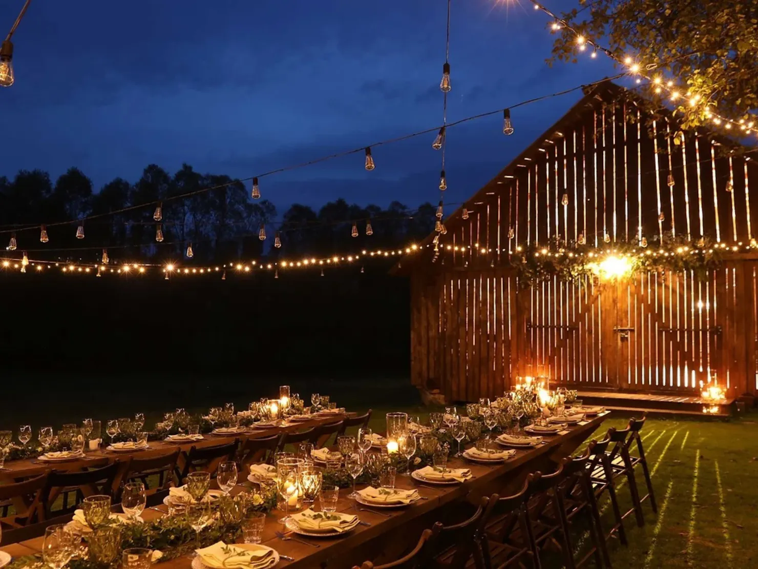 A long table in the back yard with hanging lights.