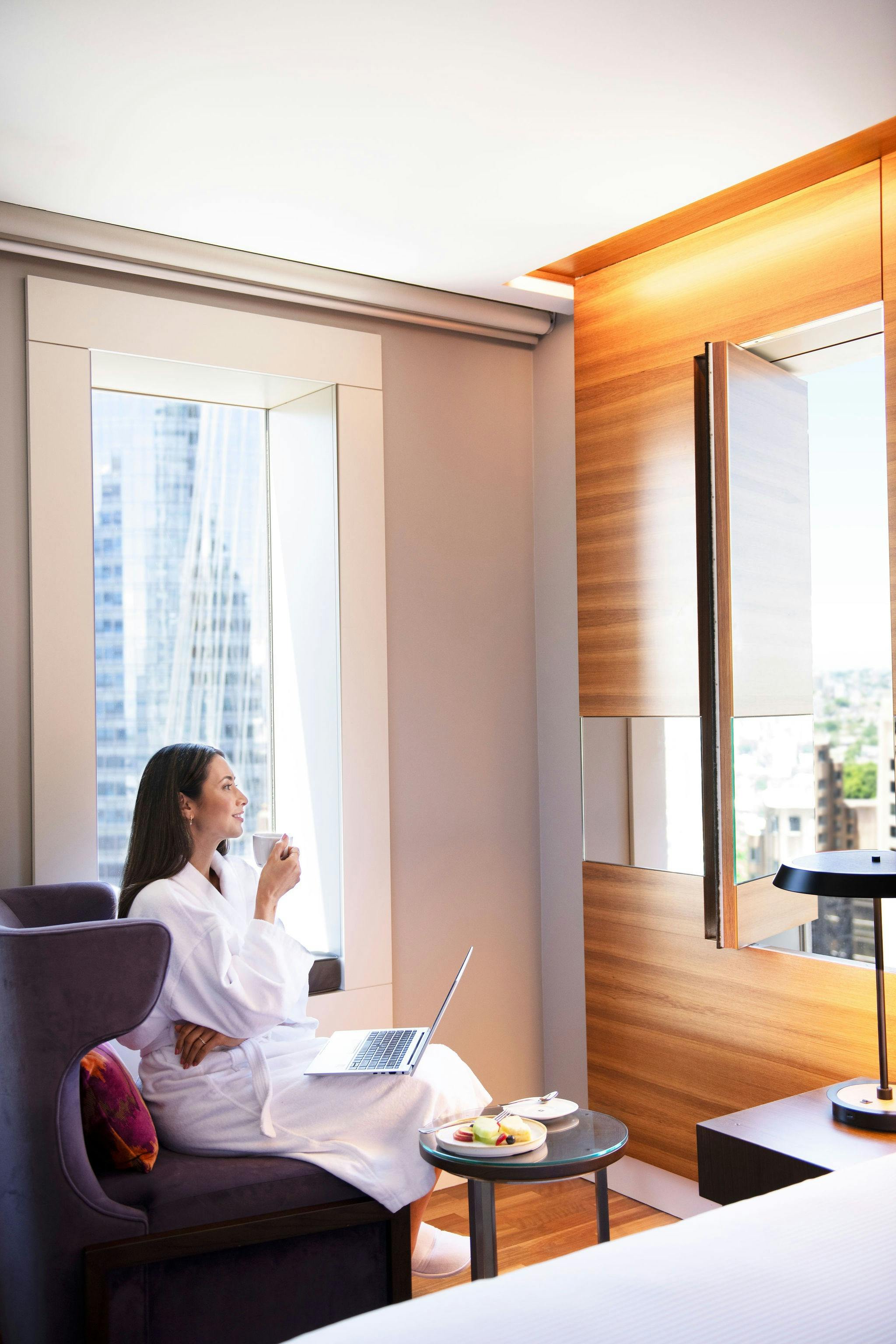 A female guest sits in the corner of her City View Suite, with her laptop and a coffee.
