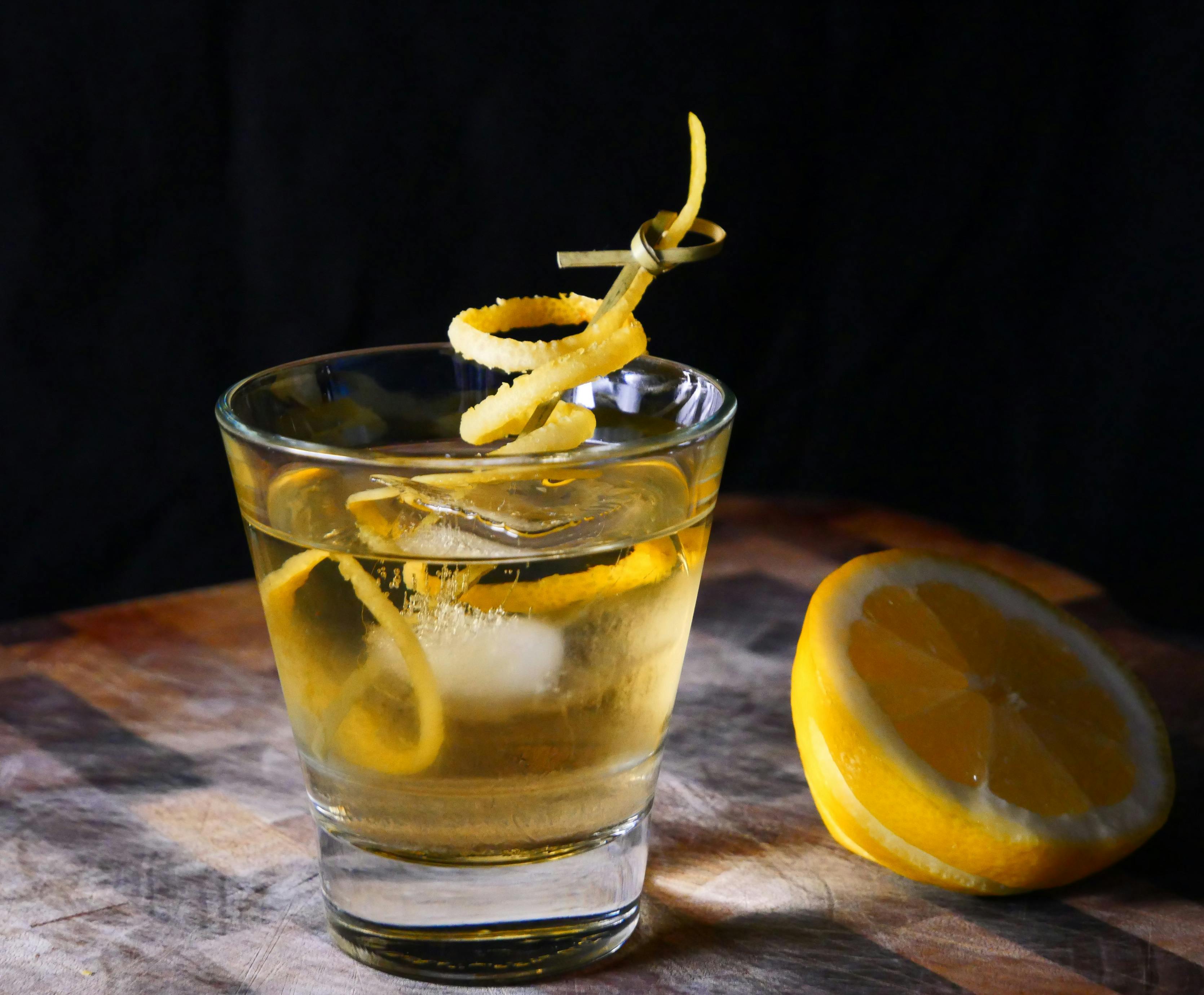 Yellow Cocktail with ice and a lemon twist.