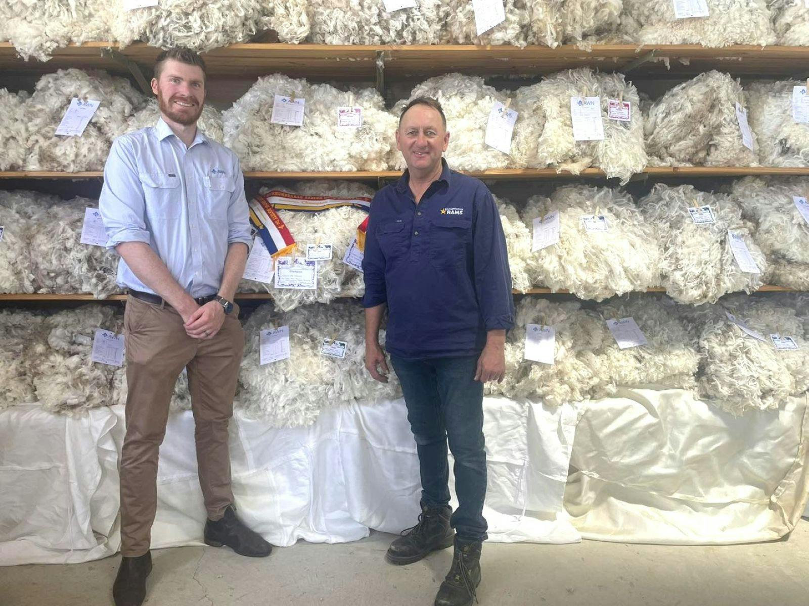 Wool quality winner and judge in front of a wall of all sorts of shorn wool entries.
