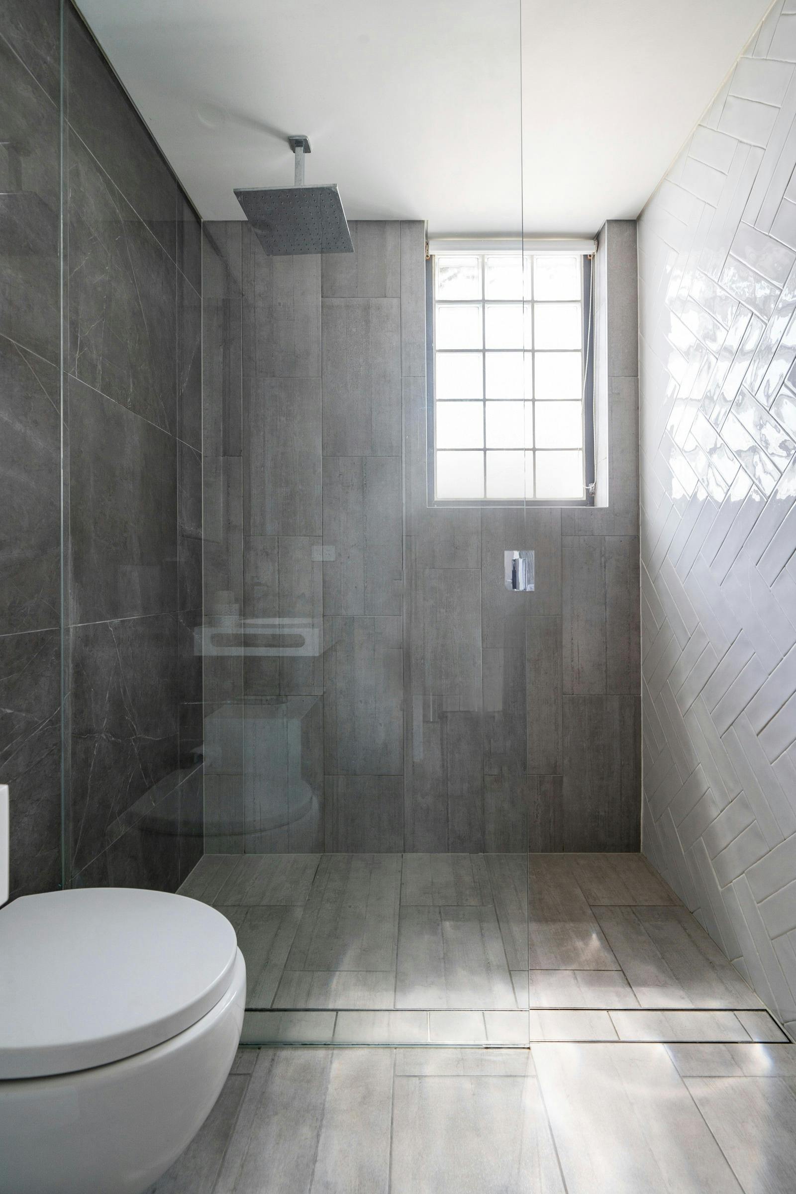 大きなシャワーとモダンなグレーのタイルが備わった広々としたバスルーム。