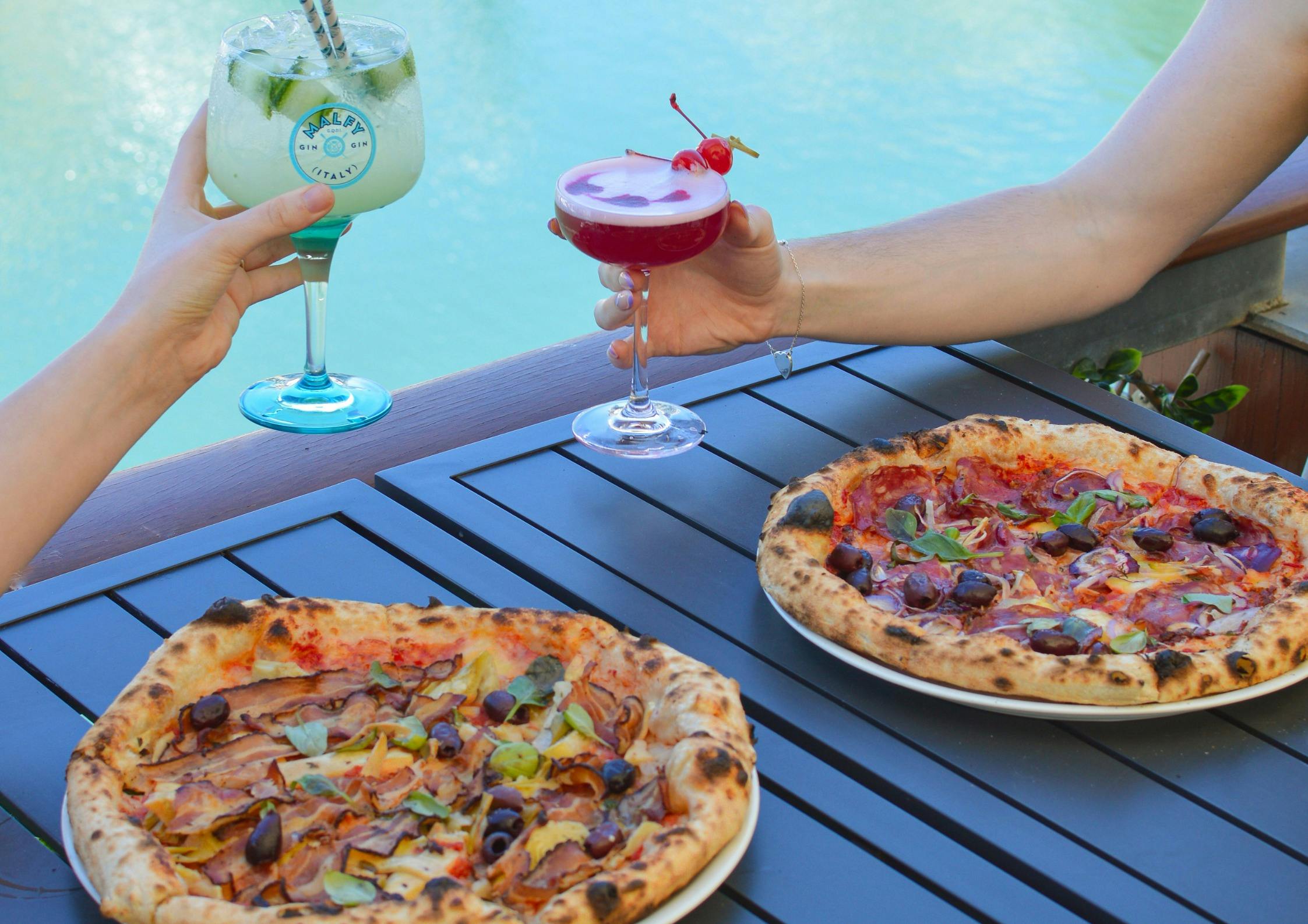 two people enjoying pizzas and cocktails by the marina water