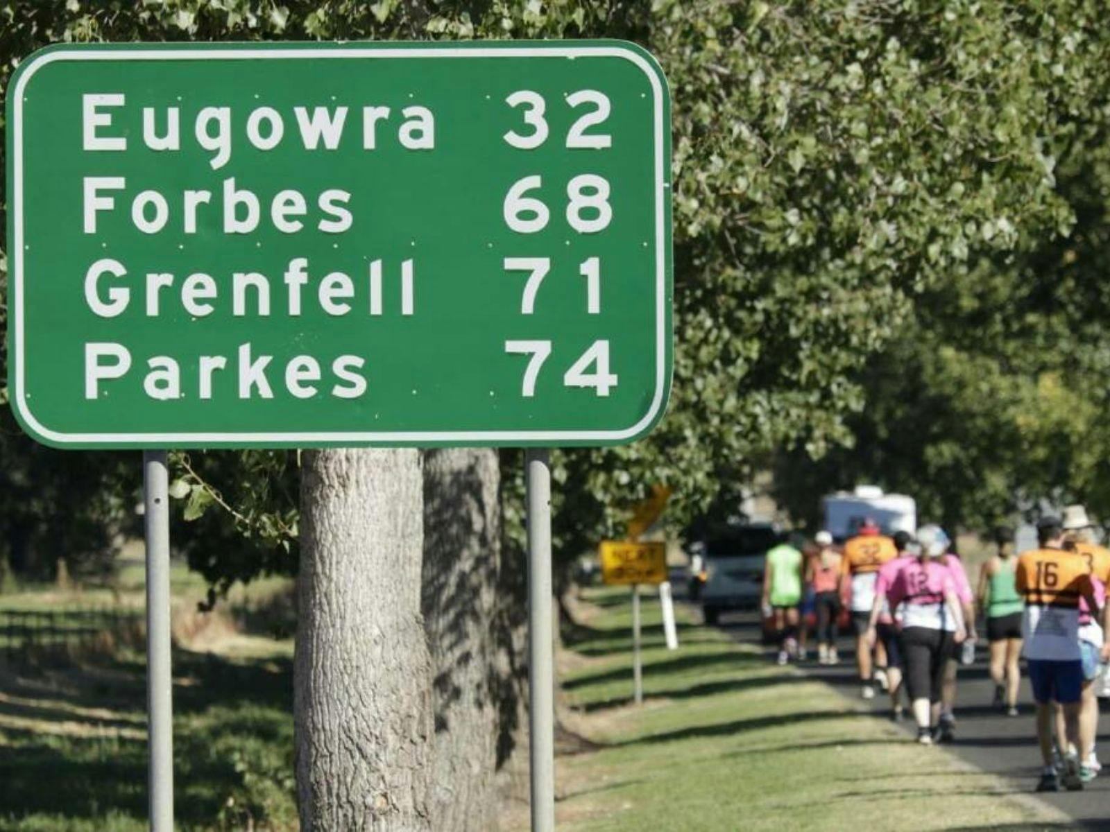 People walking on road behind roadsign to Grenfell