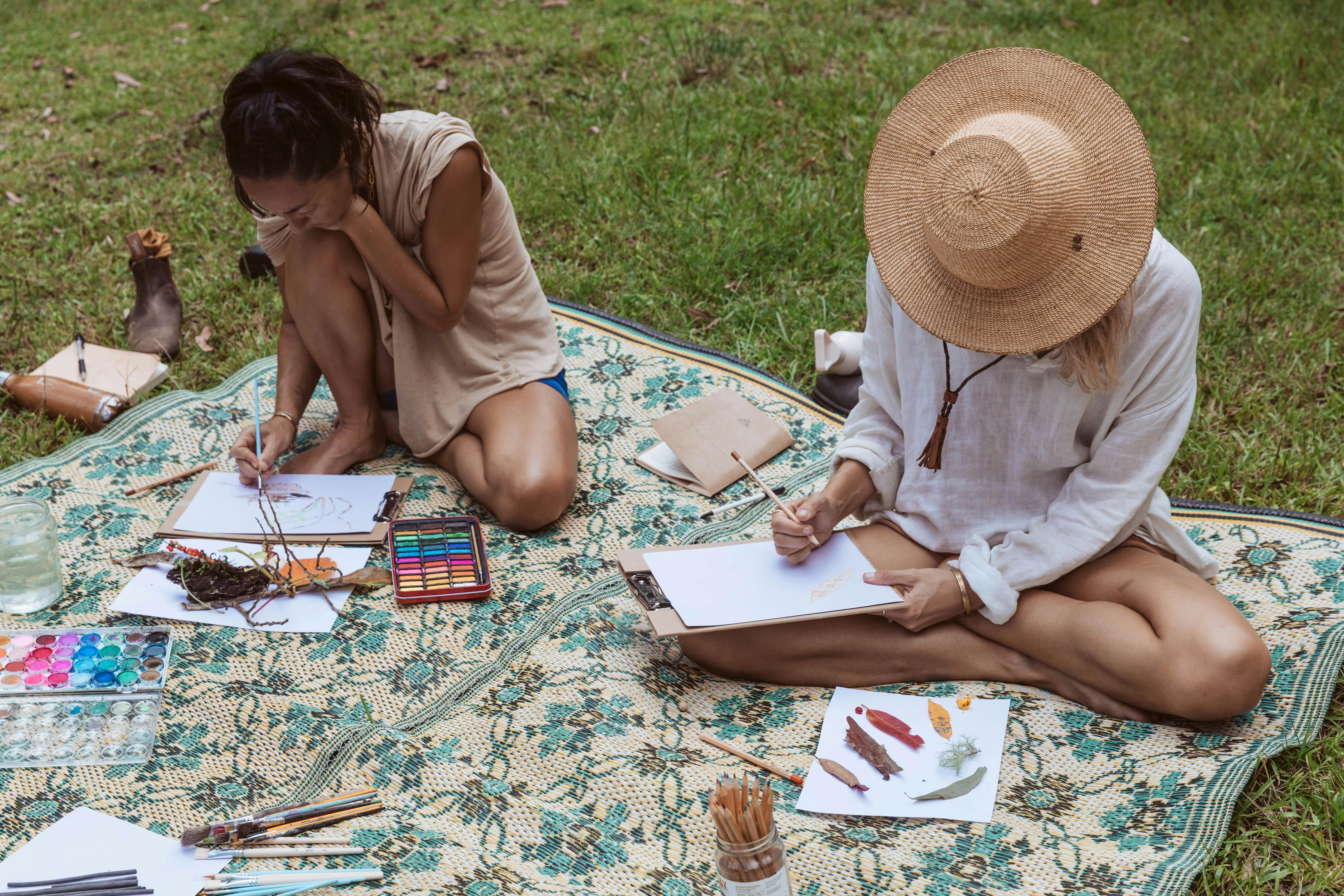 To people sitting on a mat, painting and drawing with found nature objects in front of them
