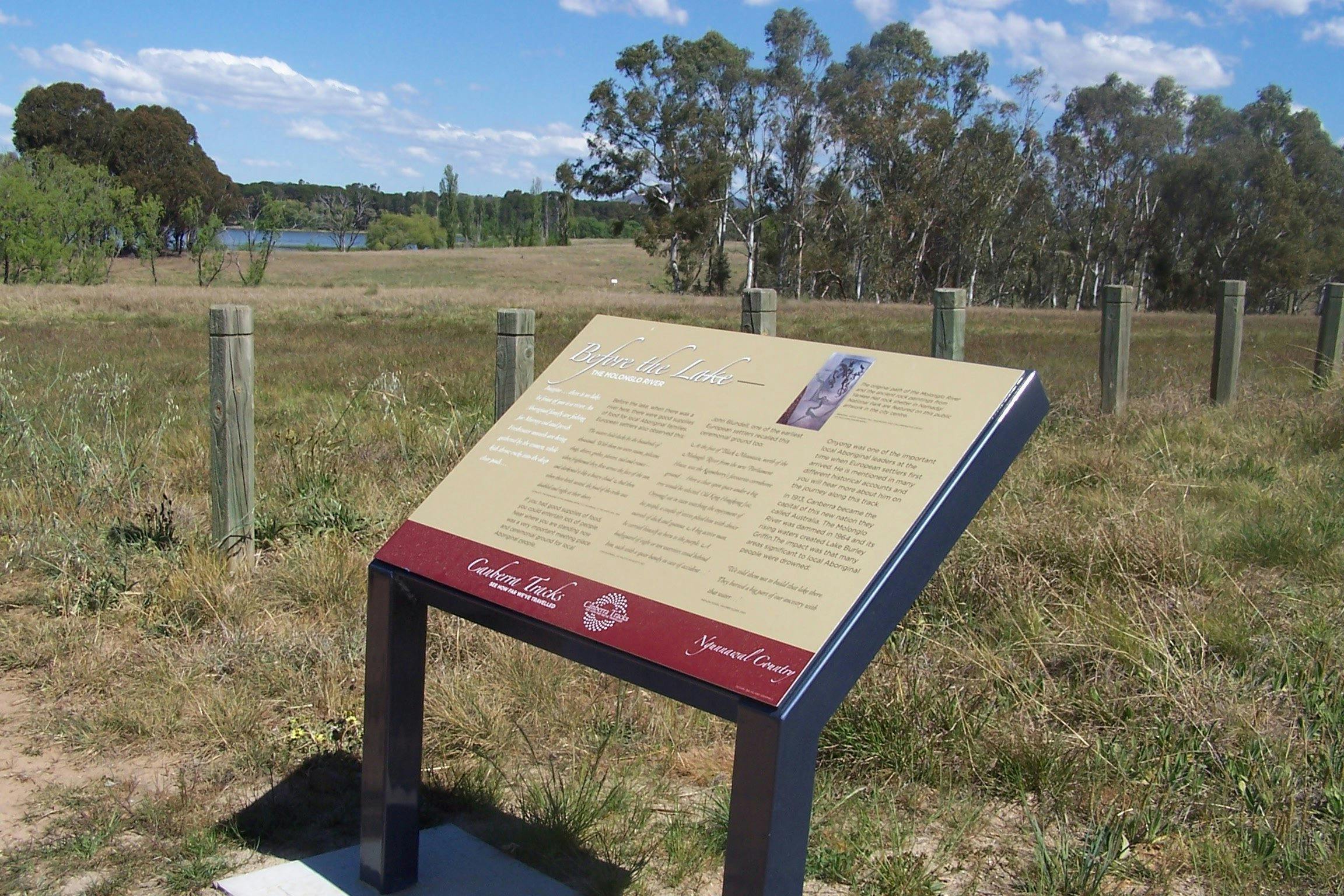 Information board in grassed area with fence and water in background