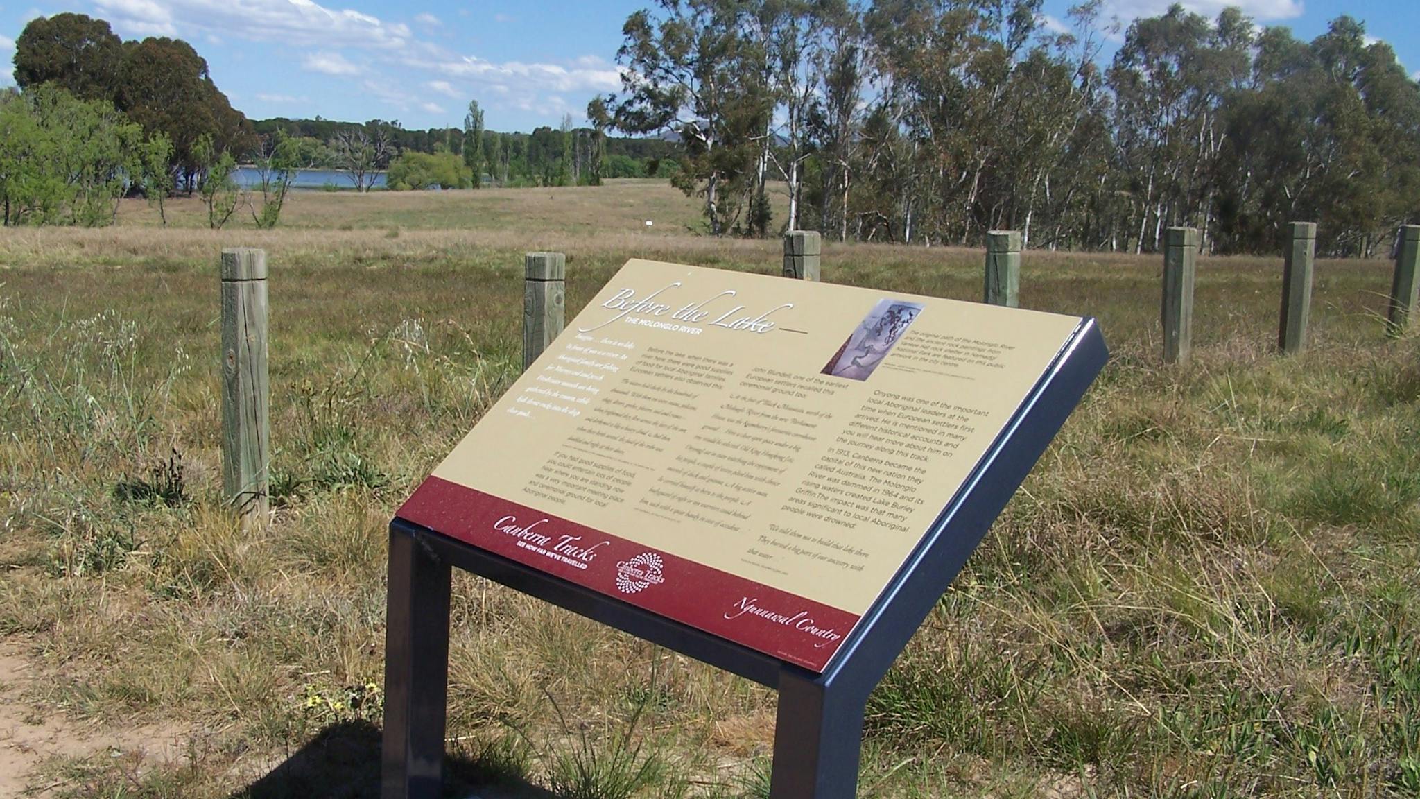 Information board in grassed area with fence and water in background