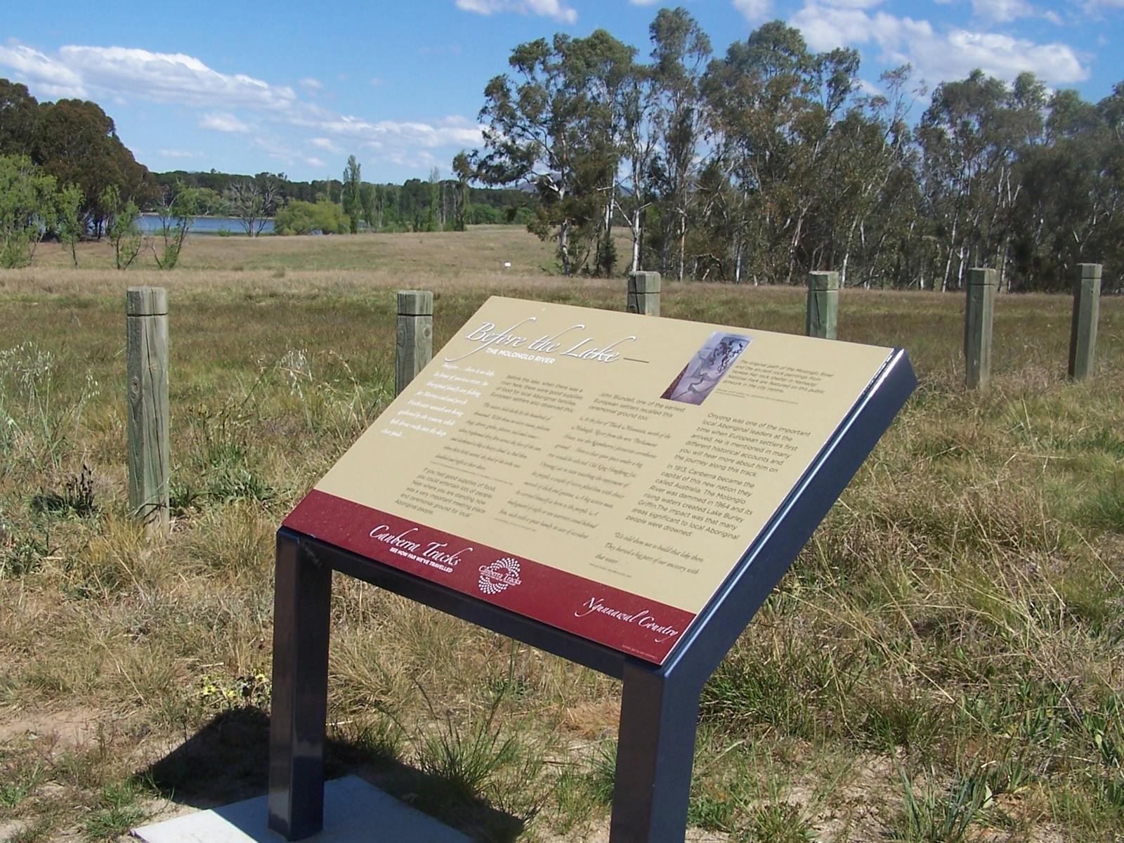 Information board in grassed area with fence and water in background