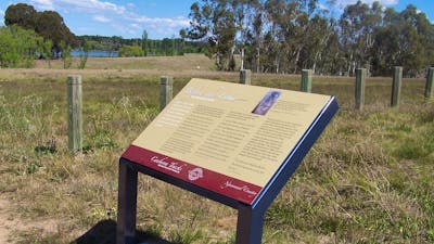 Information board in grassed area with fence and water in background