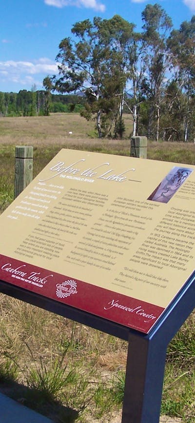 Information board in grassed area with fence and water in background