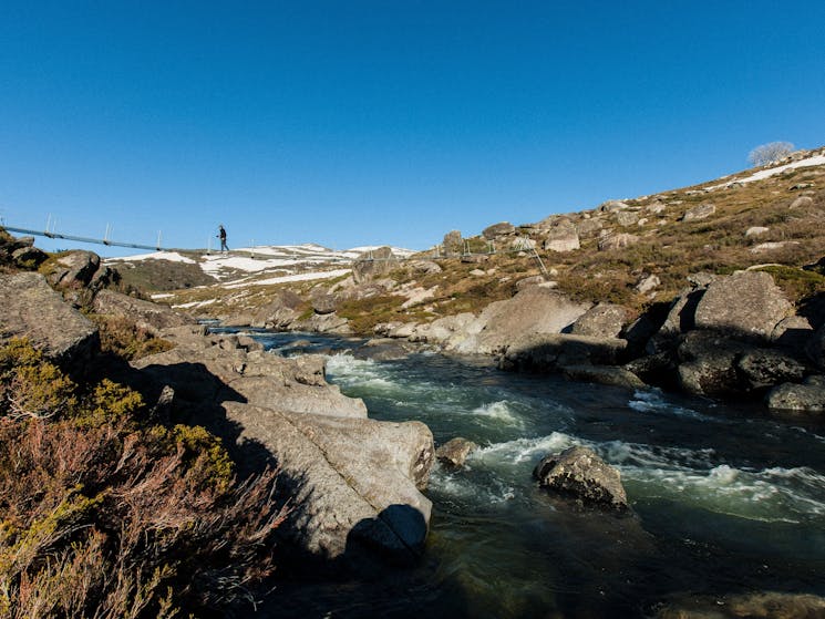 A person walking on a bridge over a stream in  the Snowy Mountains