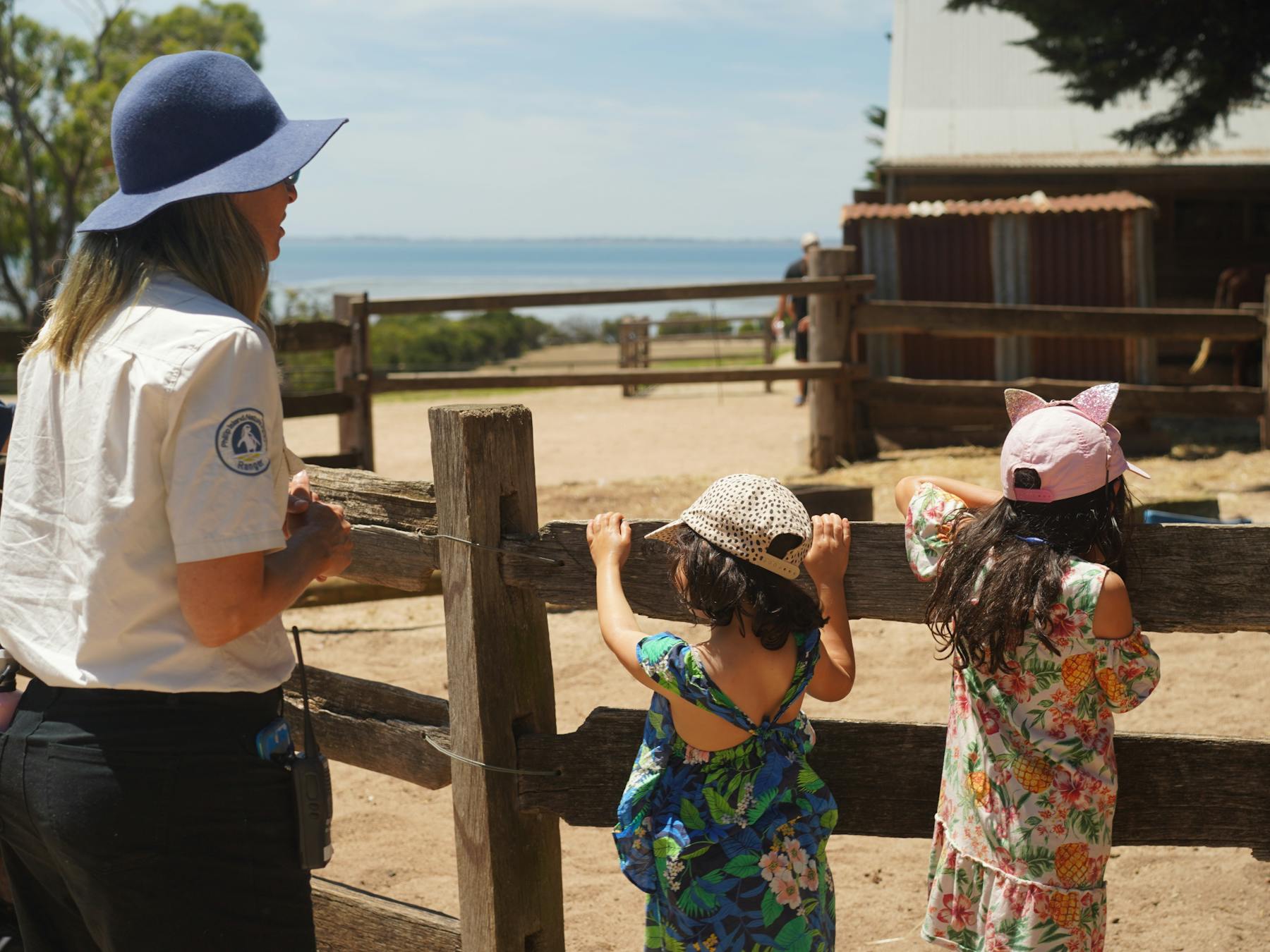 Churchill Island ranger with two children looking away from camera into a fenced paddock.