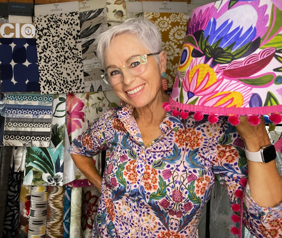 picture of grey-haired lady smiling and holding up colourful lampshade