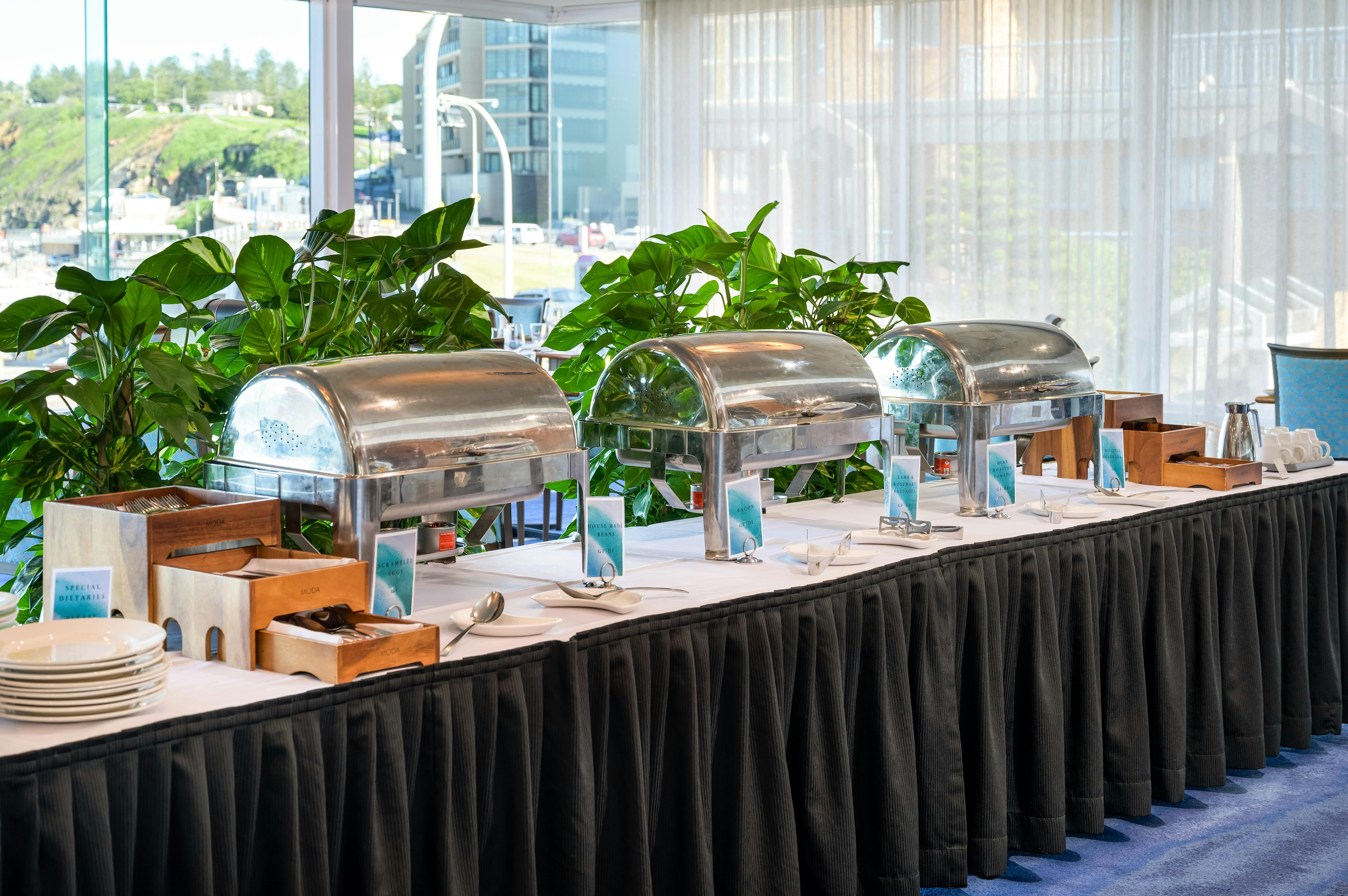 Buffet breakfast setup of hot food and cutlery and view of Newcastle Beach