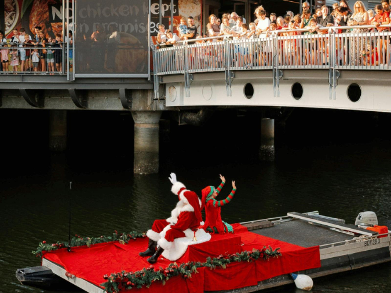 Santa and elf waving to crowd from a boat at the Sunshine Plaza Riverwalk precinct