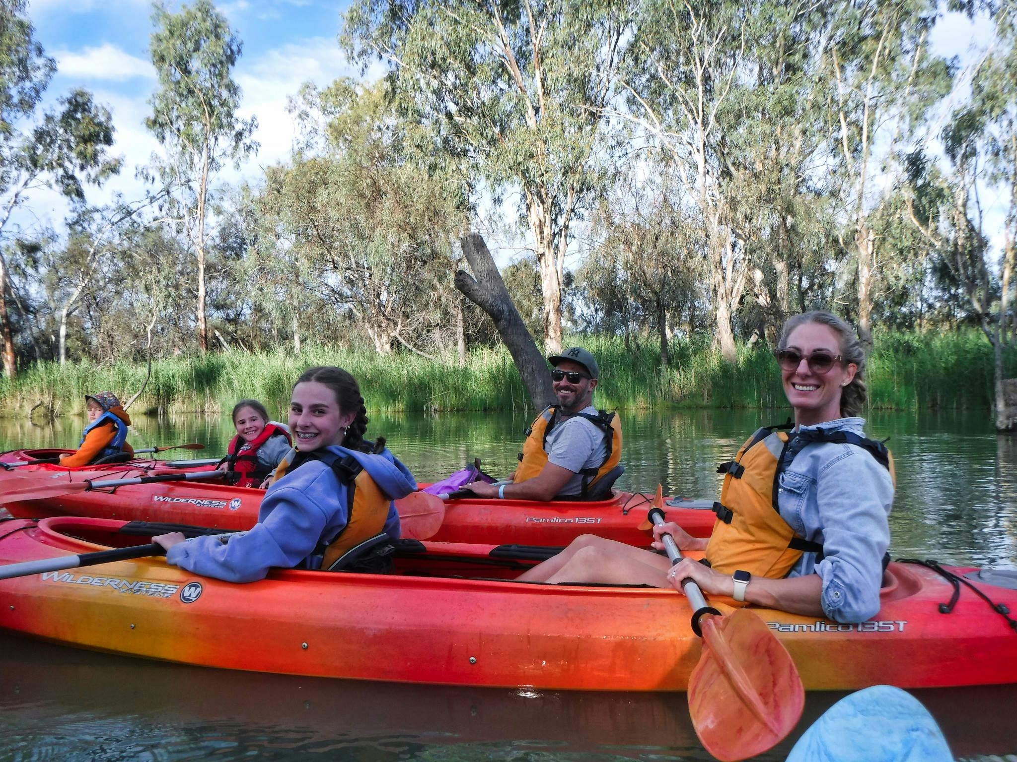 Smiling family paddling along tree-lined creek.