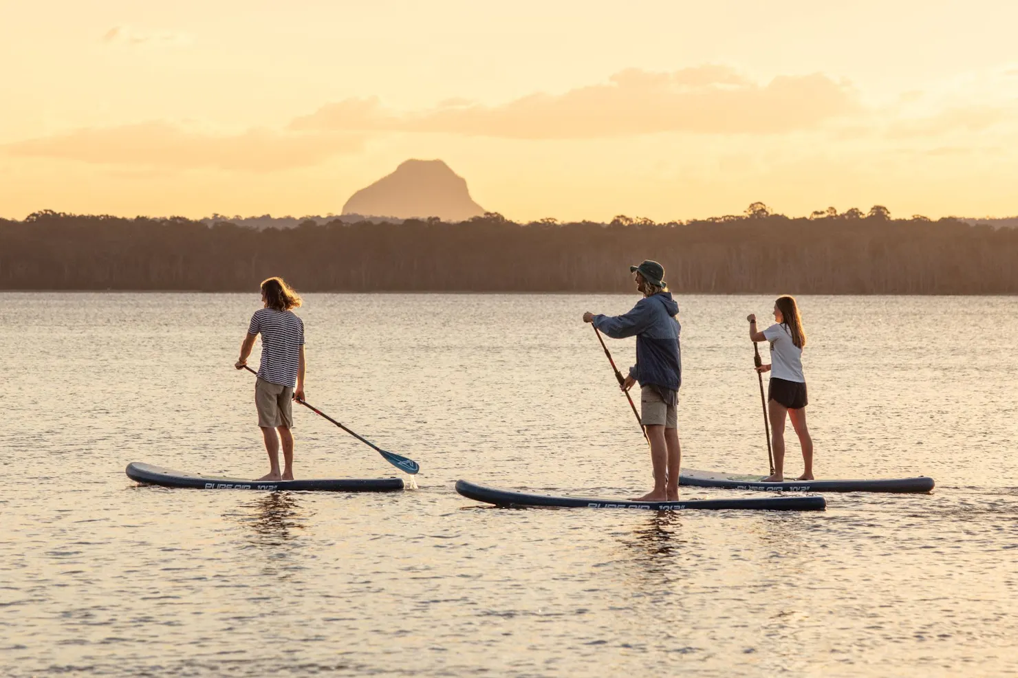 Three people on Stand Up Paddle boards on Lake Cootharaba during sunset