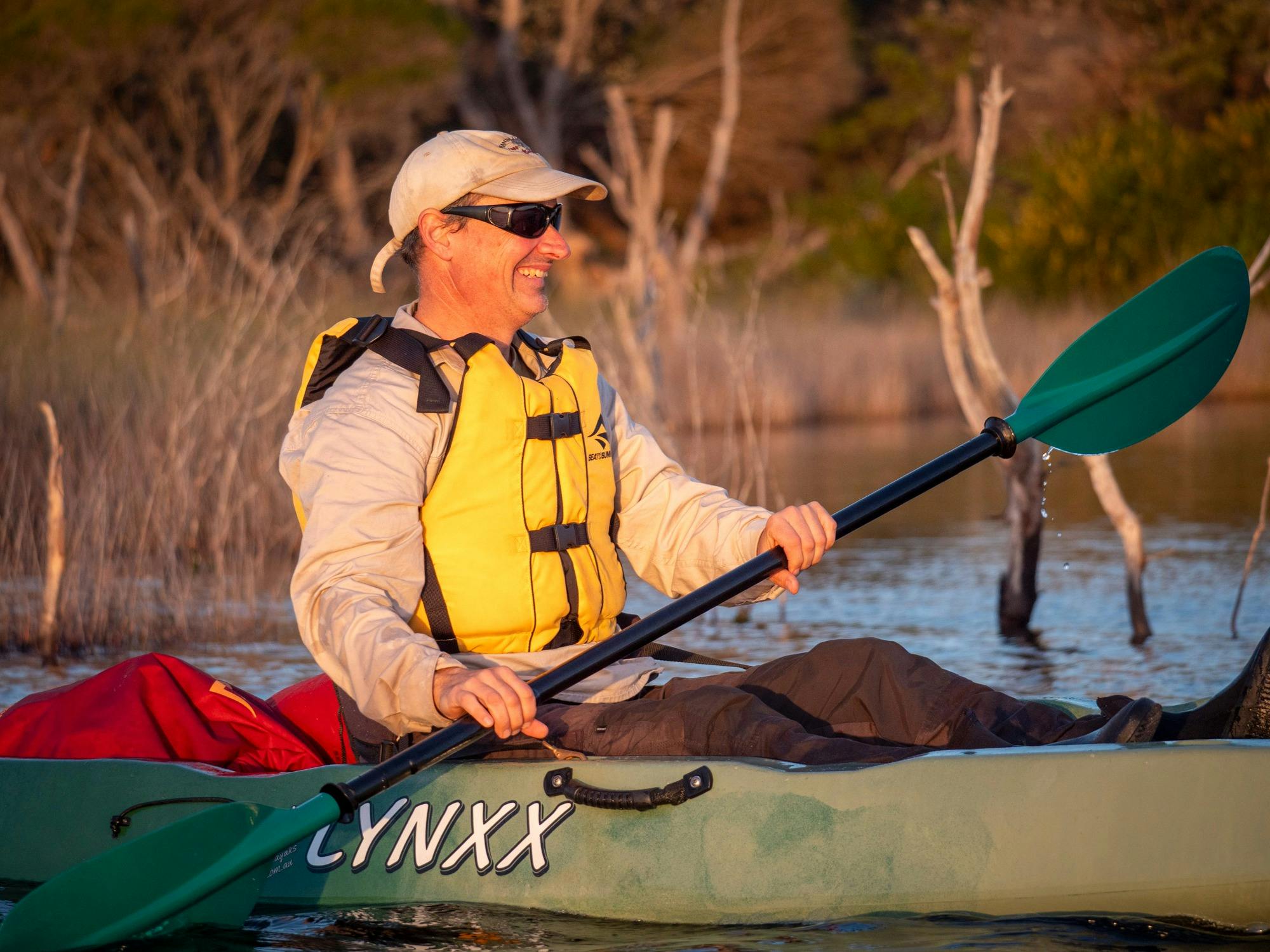 Close-up portrait of a person in a kayak, smiling brightly as their face is bathed in the warm, gold