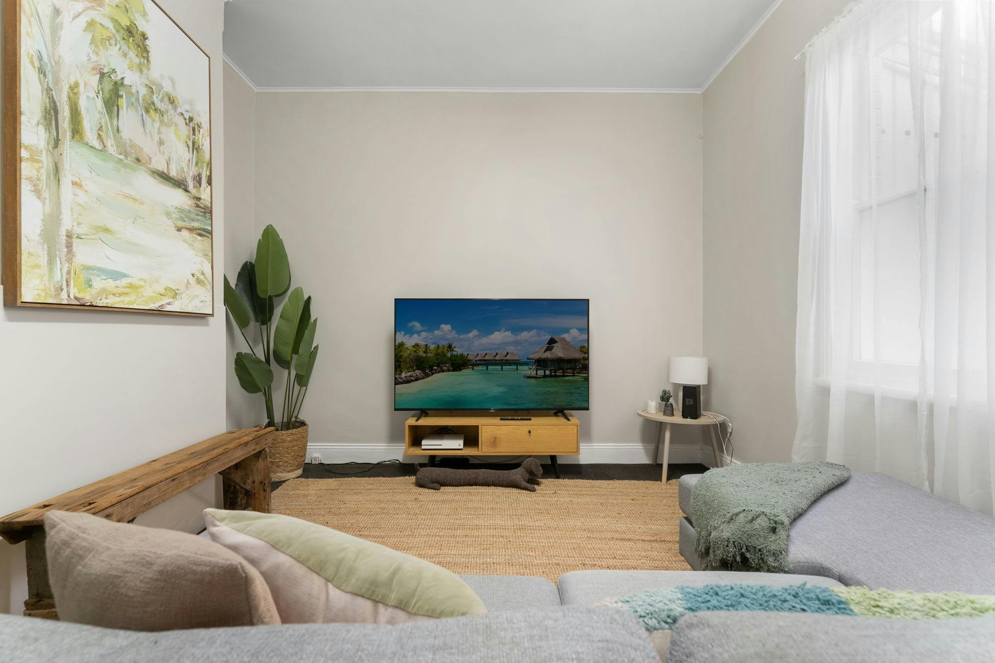 Lounge with large couch, tv and tv entertainment unit, fake plant, art on the wall, brown rug