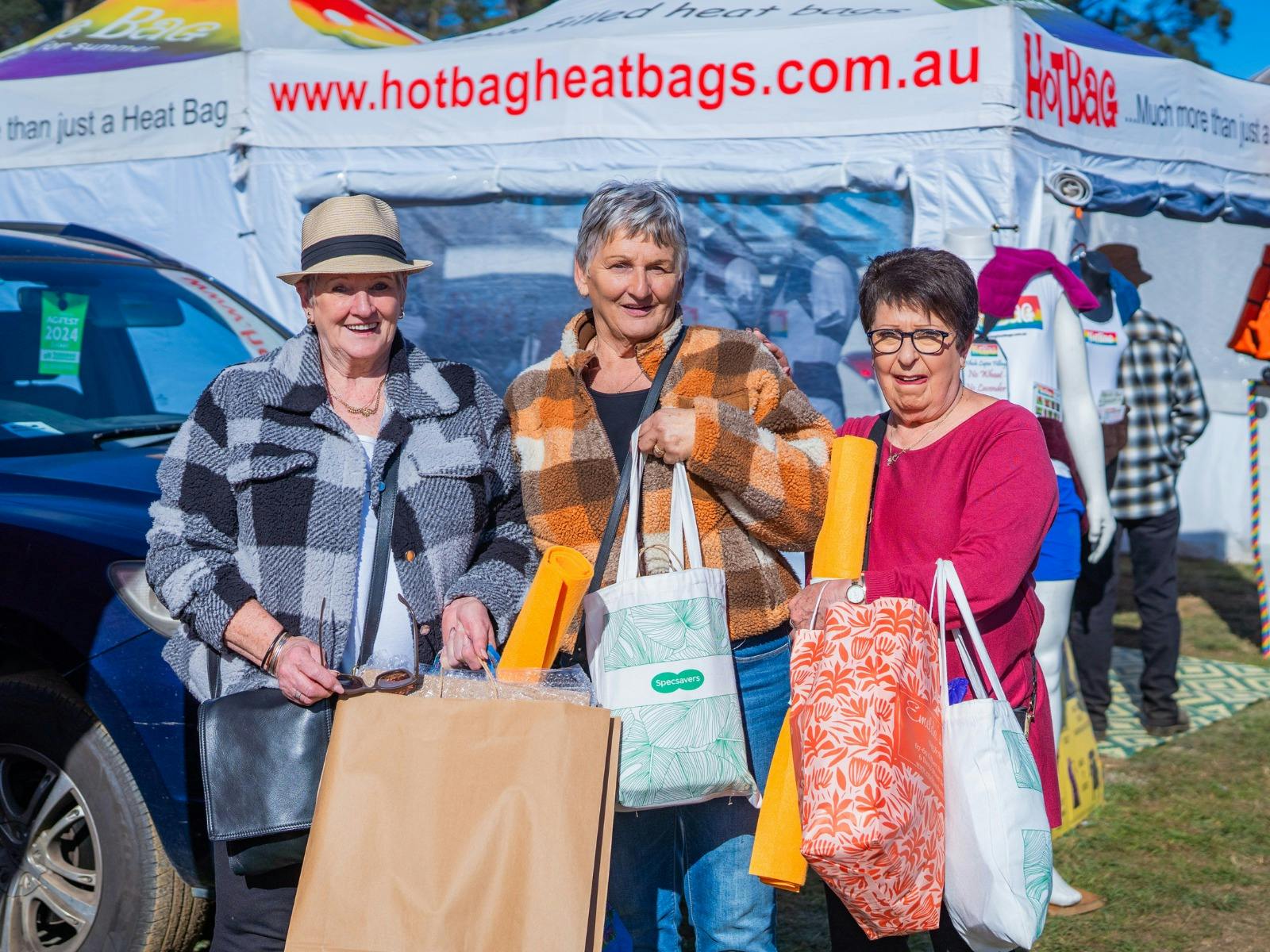 Three women smile, holding their Agfest shopping bags filled with local goods