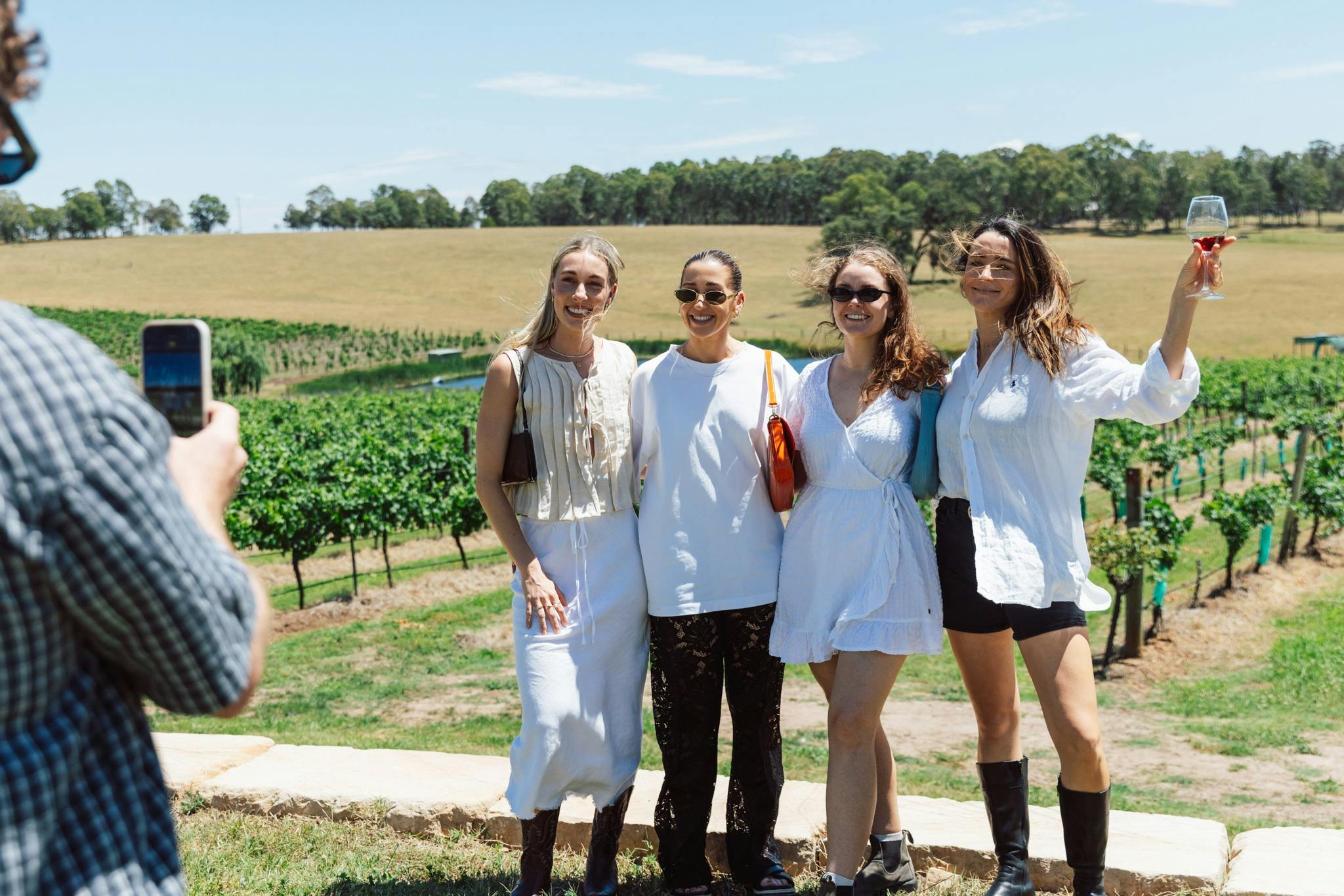 A man taking a photo of 4 women in front of vineyard