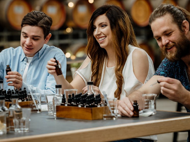 Three people sit at a table with beakers and droppers, blending their own spirits