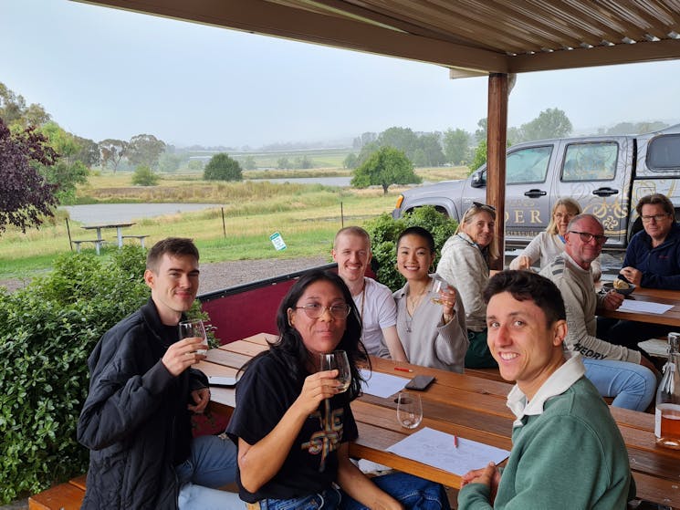 A group of people tasting cider on the veranda of Small Acres Cyder with views of the dam.