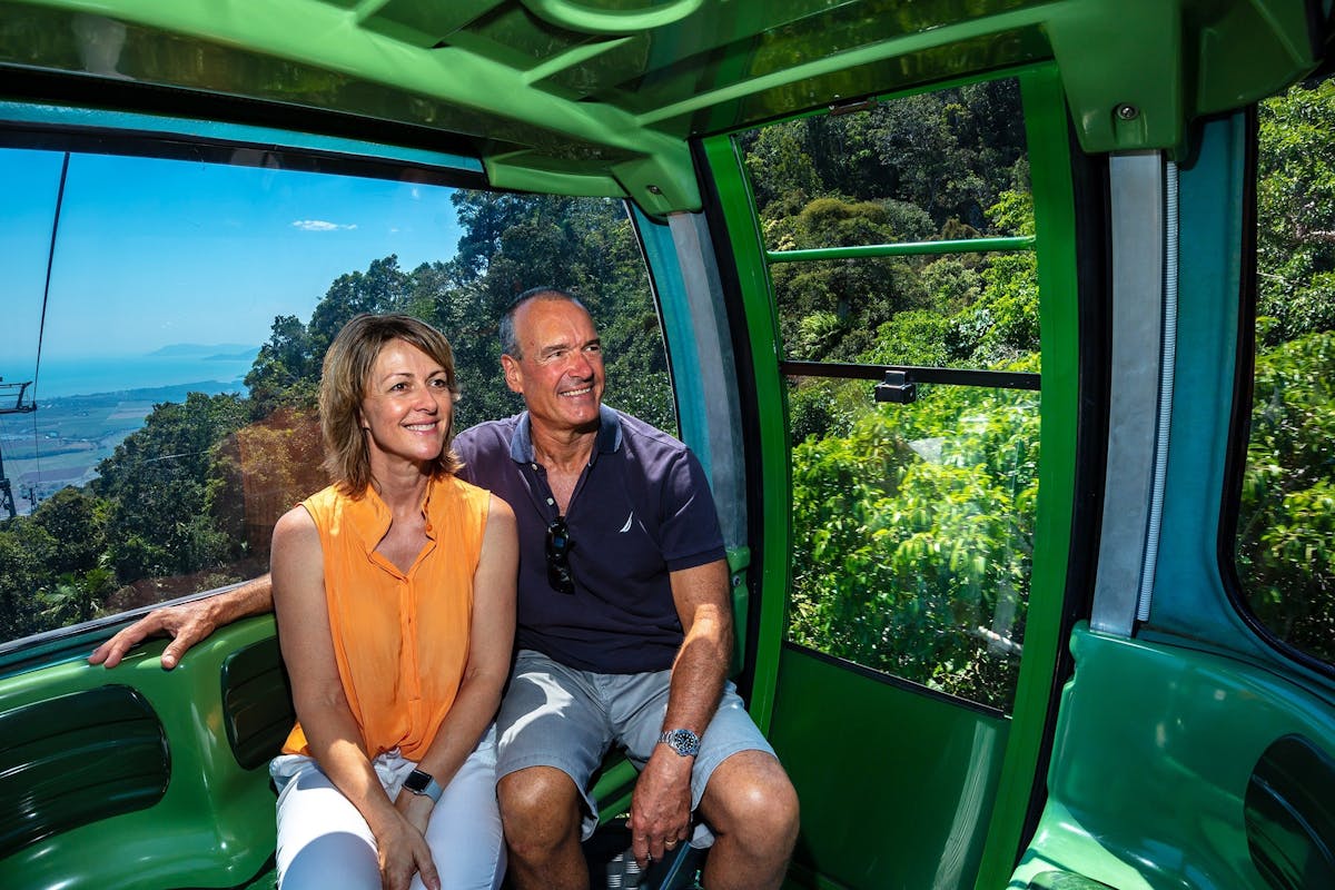 Two people sitting in Skyrail Rainforest Cableway gondola, enjoying scenic views.