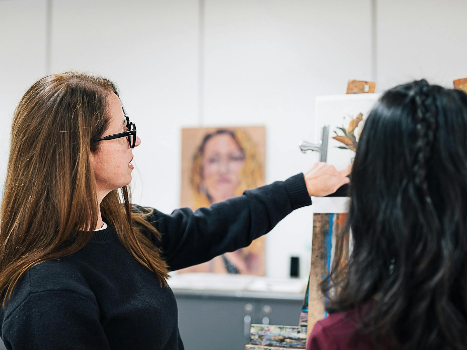 Female teacher instructing a student at a painting easel.