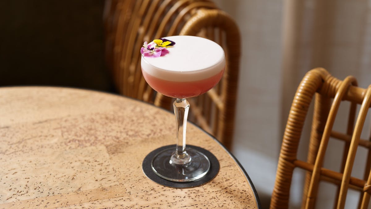 Pretty pink cocktail with floral decoration on a wooden round table in Hurricane's Surfers Paradise.