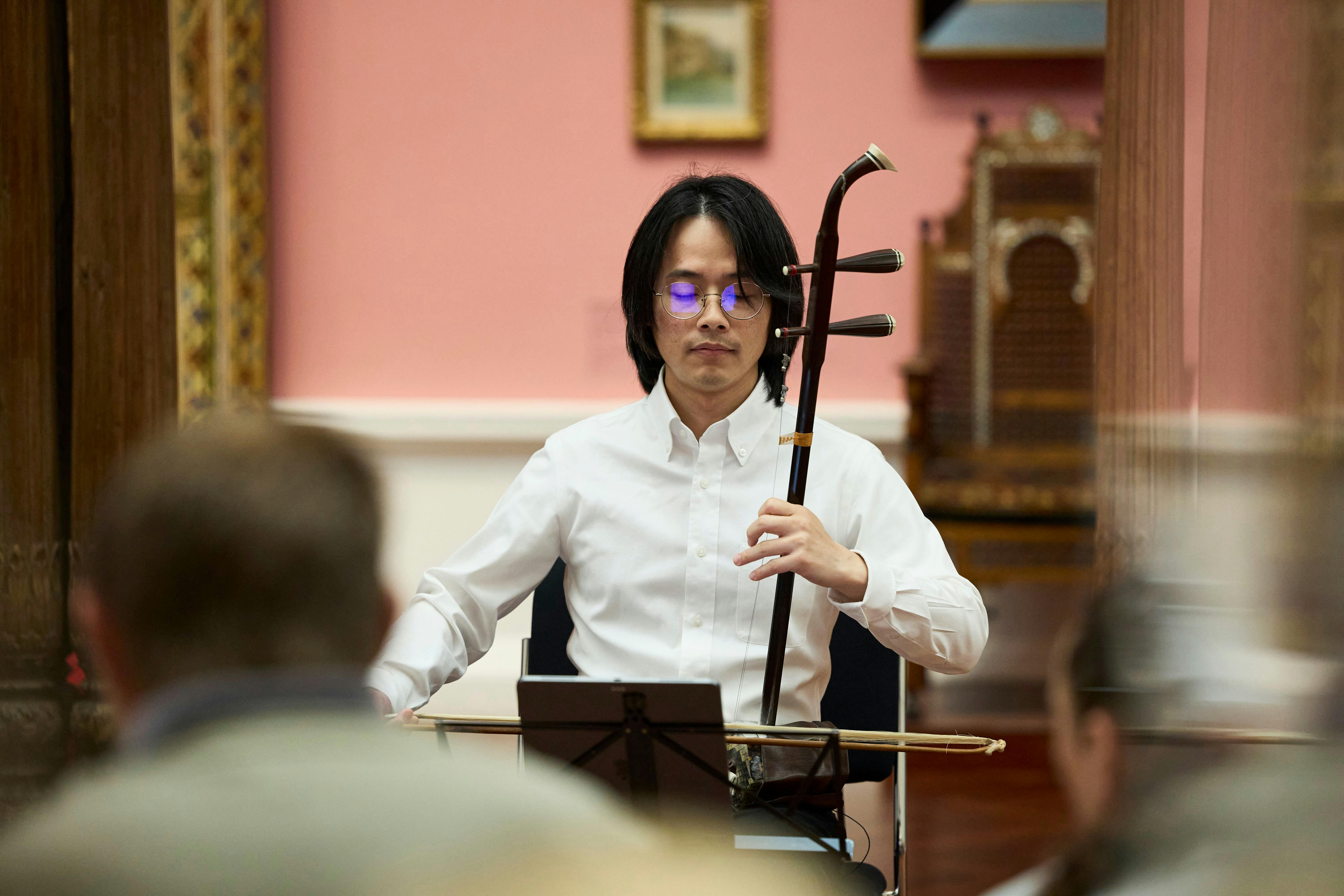 A musician plays the huqin (chinese fiddle) for an audience gathered in an art gallery.