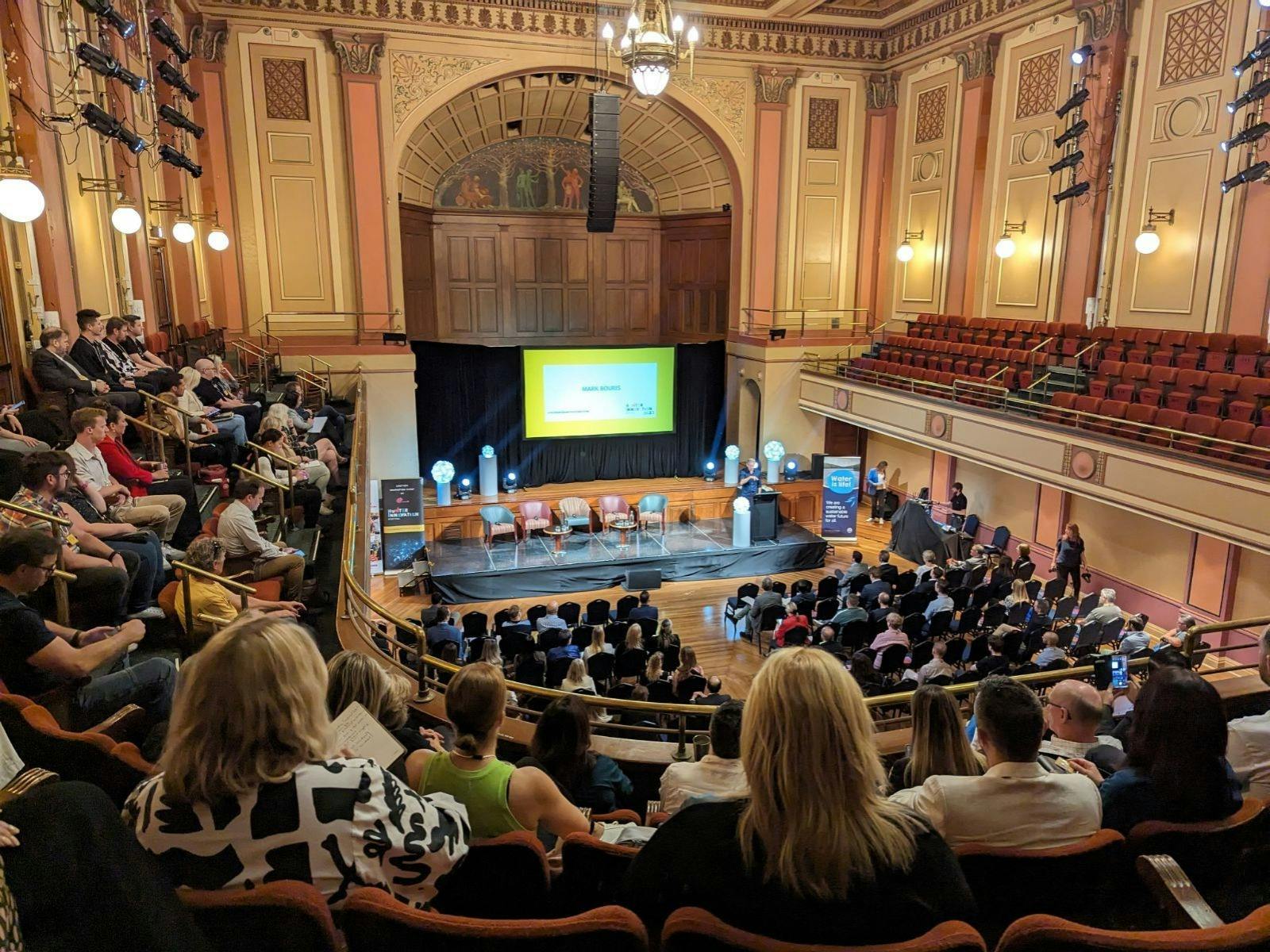 Photo of the Concert Hall taken from the gallery. The room is full of people attending a conference.