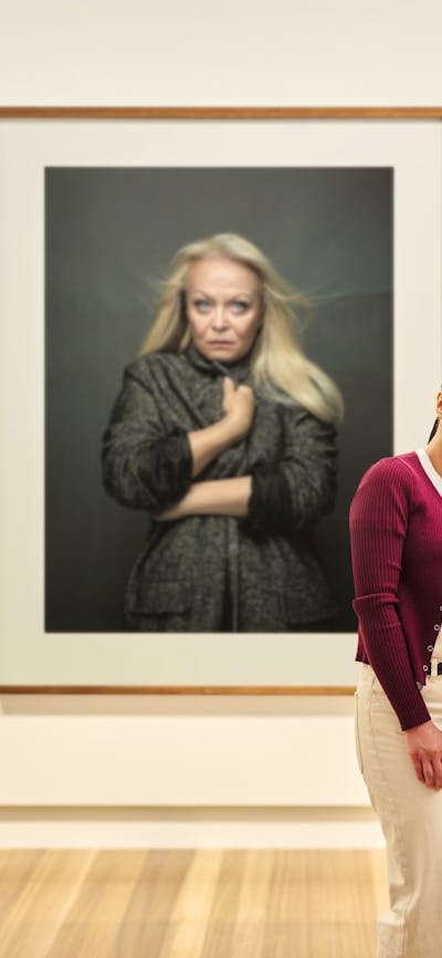 A family of three takes a selfie photo in front of a large portrait of actress Jacki Weaver.
