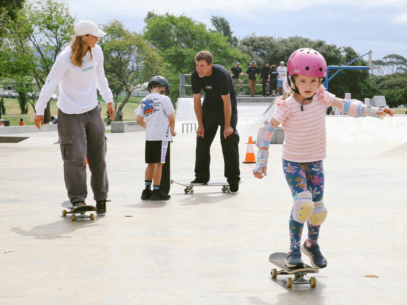 student skateboarders try to ride while watched by instructors who are also on skateboards