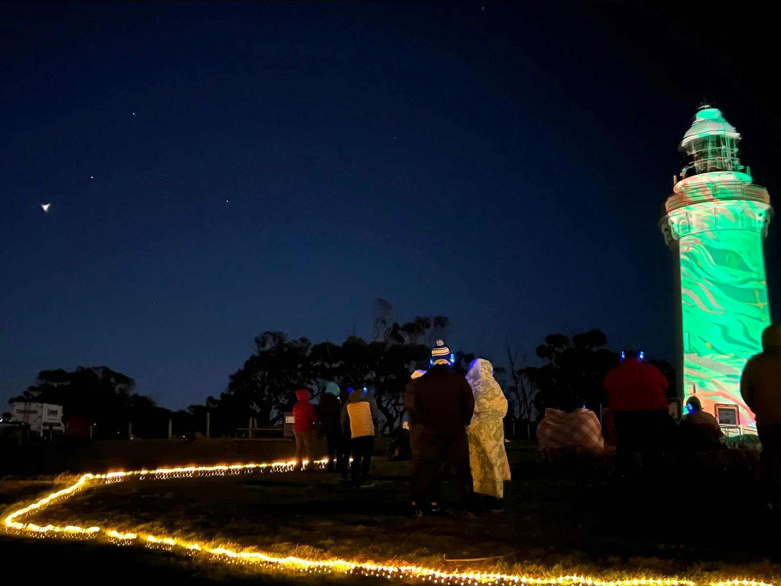 people enjoying night time projections onto to Table Cape lighhouse, wrapped up warmly.
