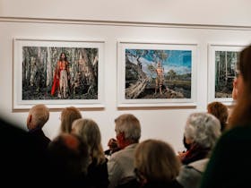 Audience sit amongst Fiona Foley's large printed photographs depicting indigenous persons