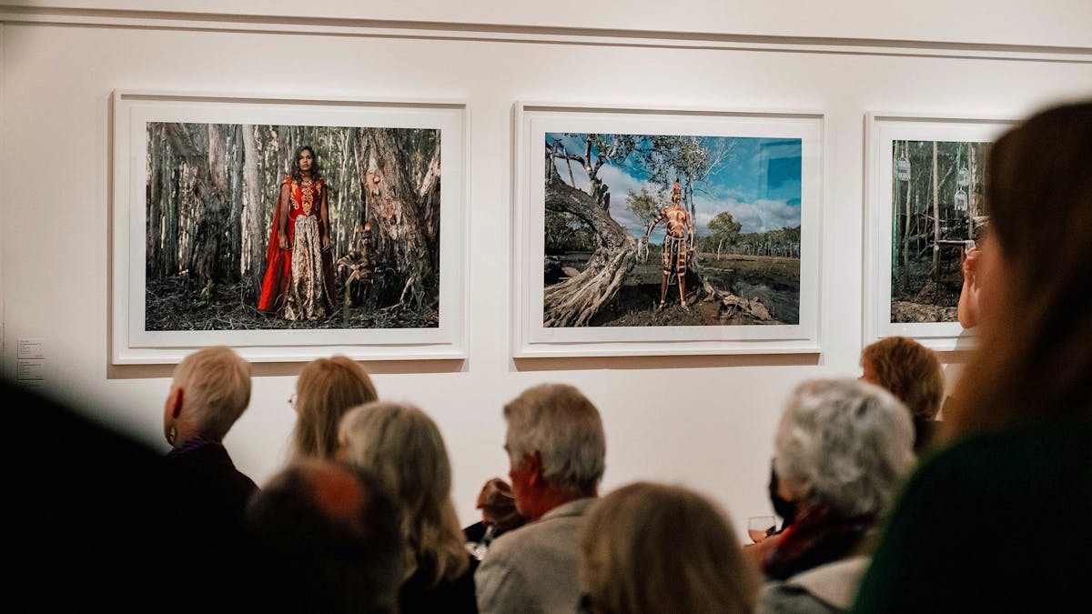 Audience sit amongst Fiona Foley's large printed photographs depicting indigenous persons
