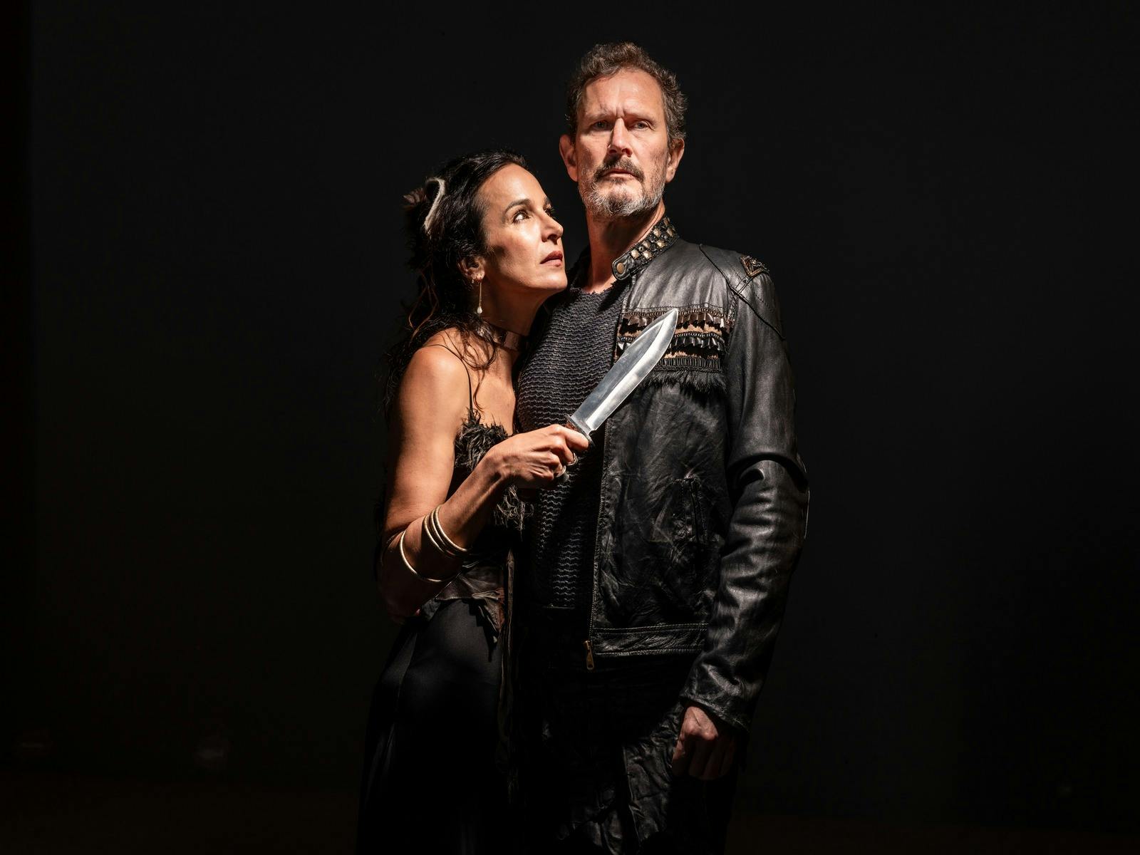 A woman holds a dagger, staring at a man in Macbeth, tension and conflict in their expressions.