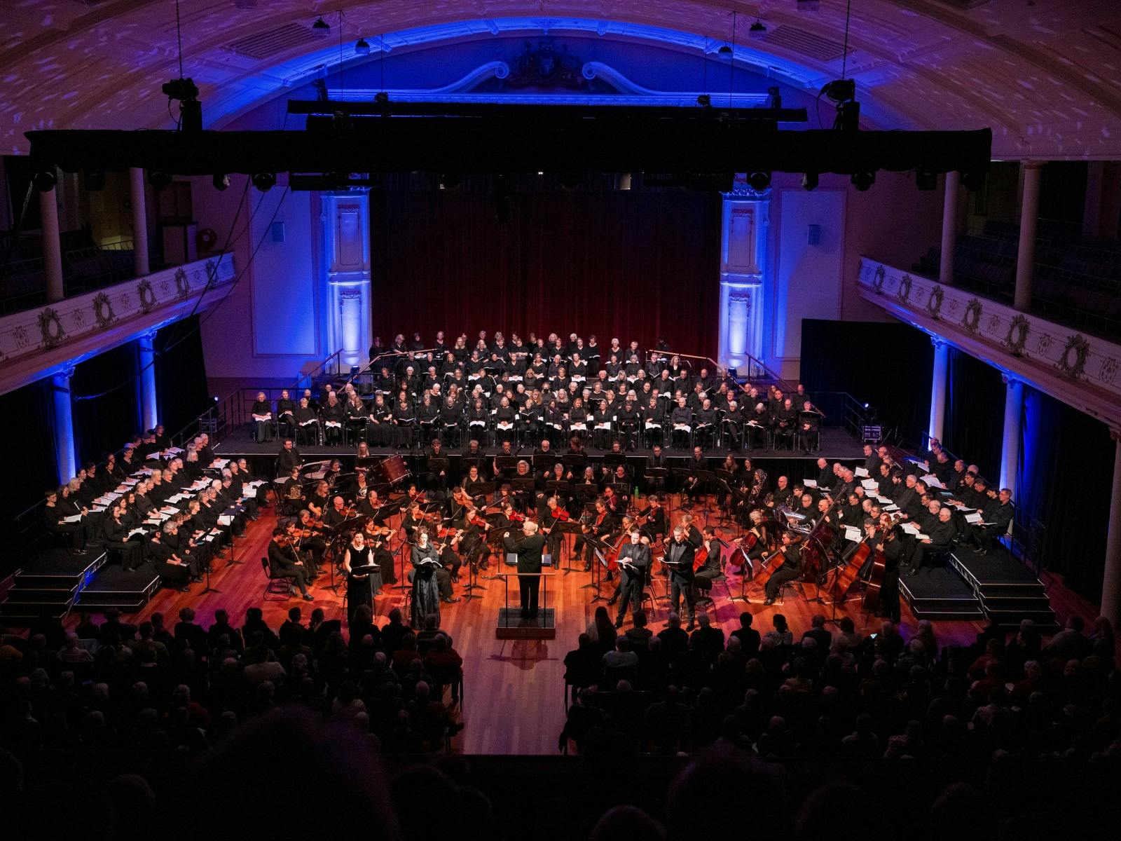 Choir and orchestra performing classical music to an audience in a concert hall.