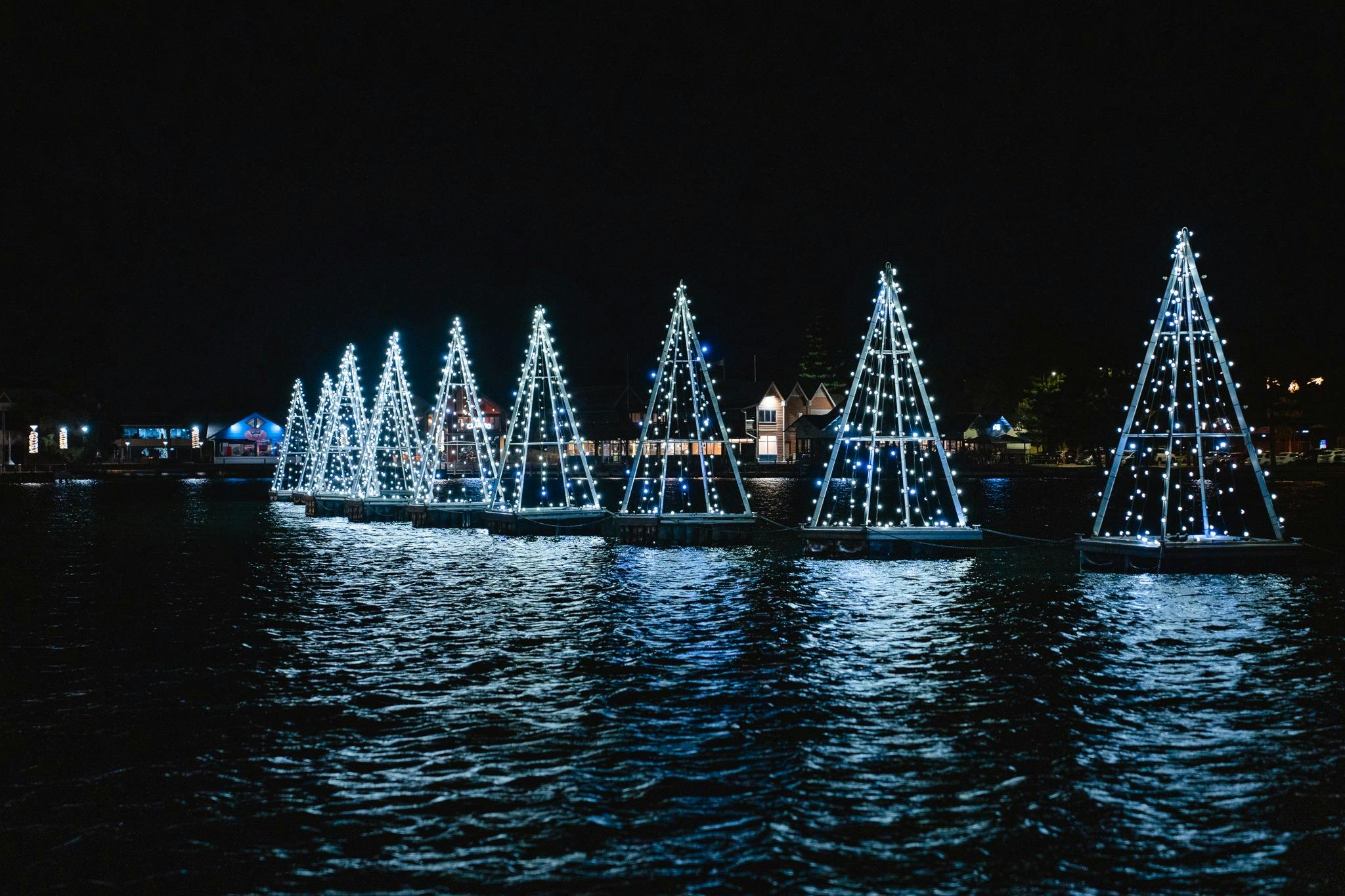 Glowing floating Christmas tree installations reflecting on the water.