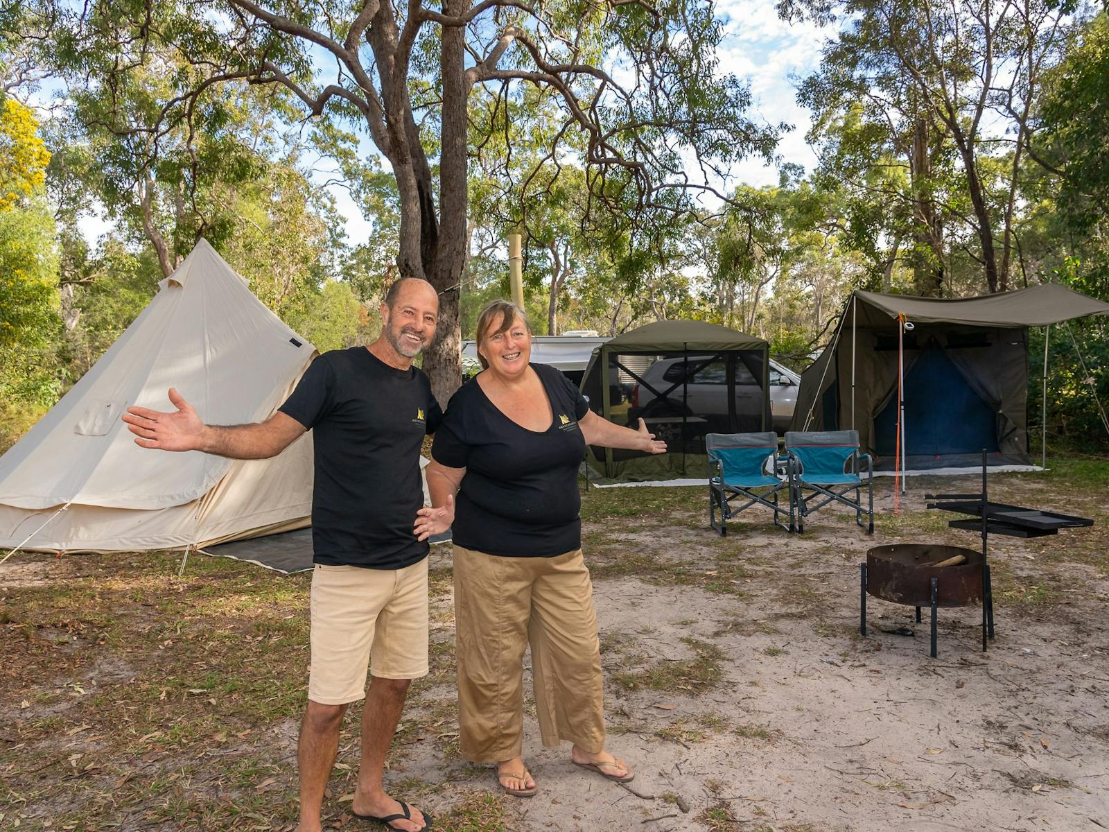 Two people standing with outstretched arms with setup camping tents behind them Two people standing with outstretched arms with setup camping tents behind them