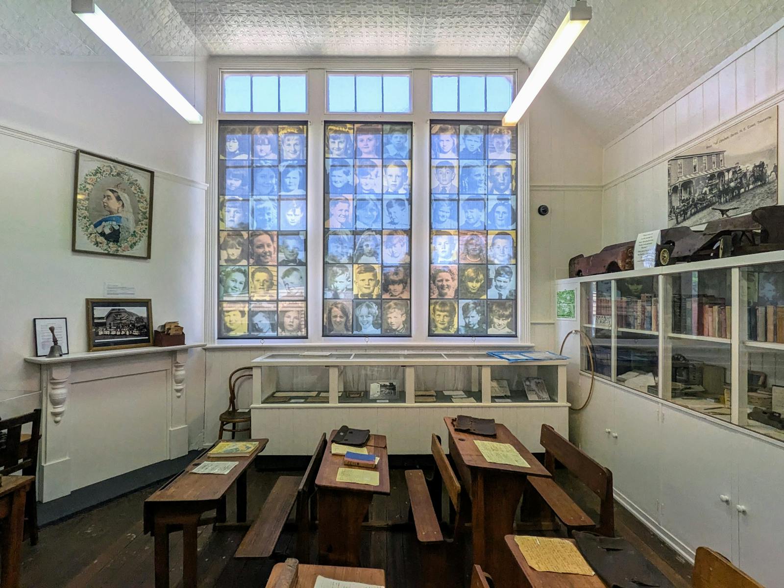 Old fashioned desks in a schoolhouse museum, with high windows showcasing prints of former students