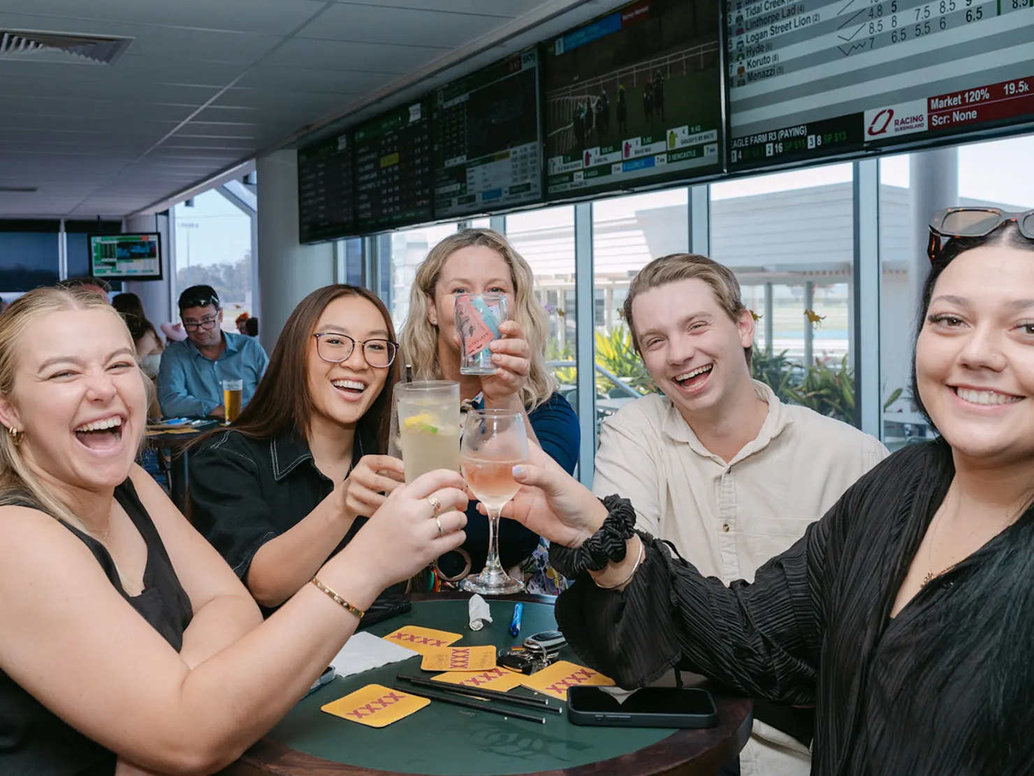 Five friends cheers-ing drinks in the middle of the table while smiling at the camera