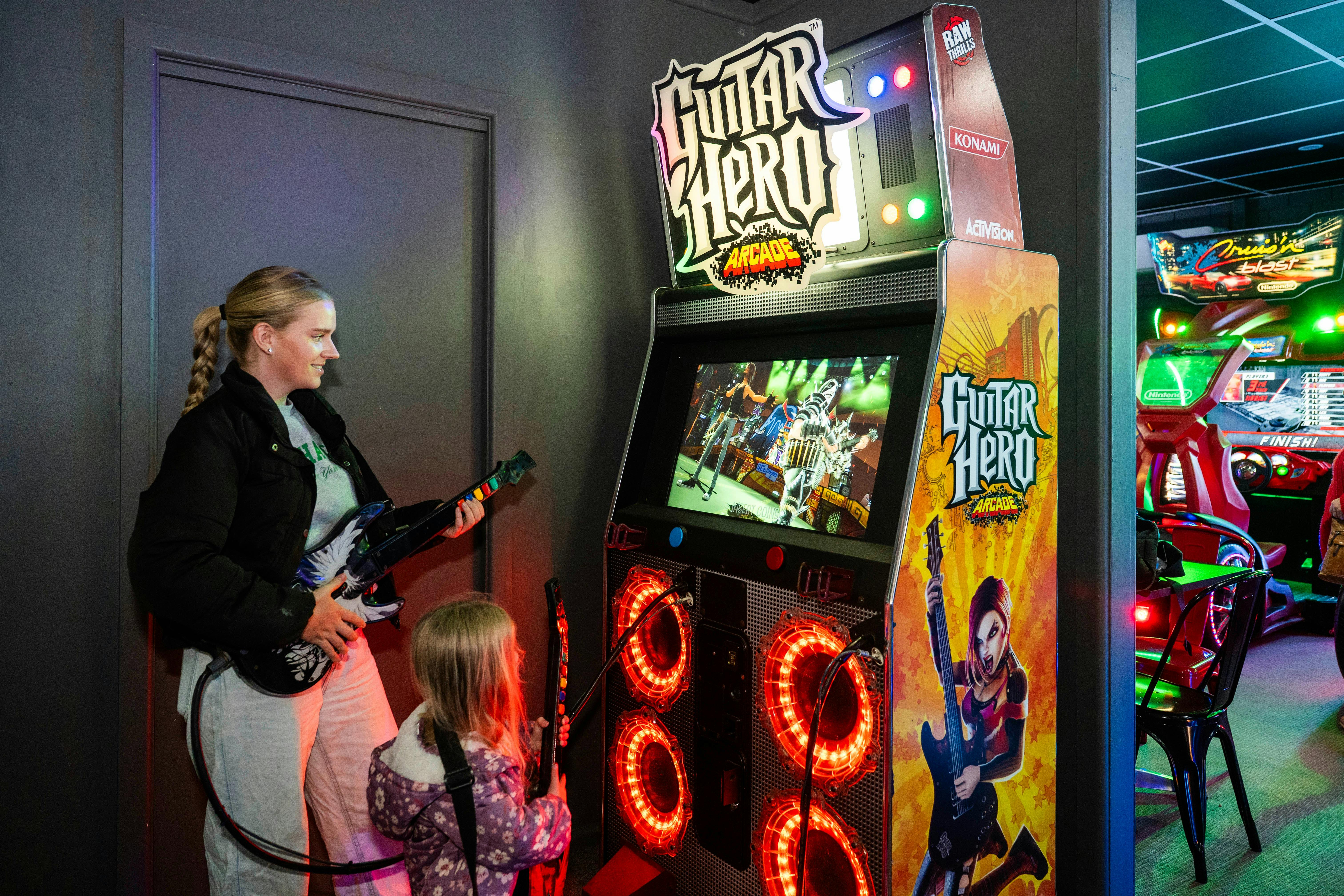 Person playing guitar hero arcade machine inside a neon-lit gaming room