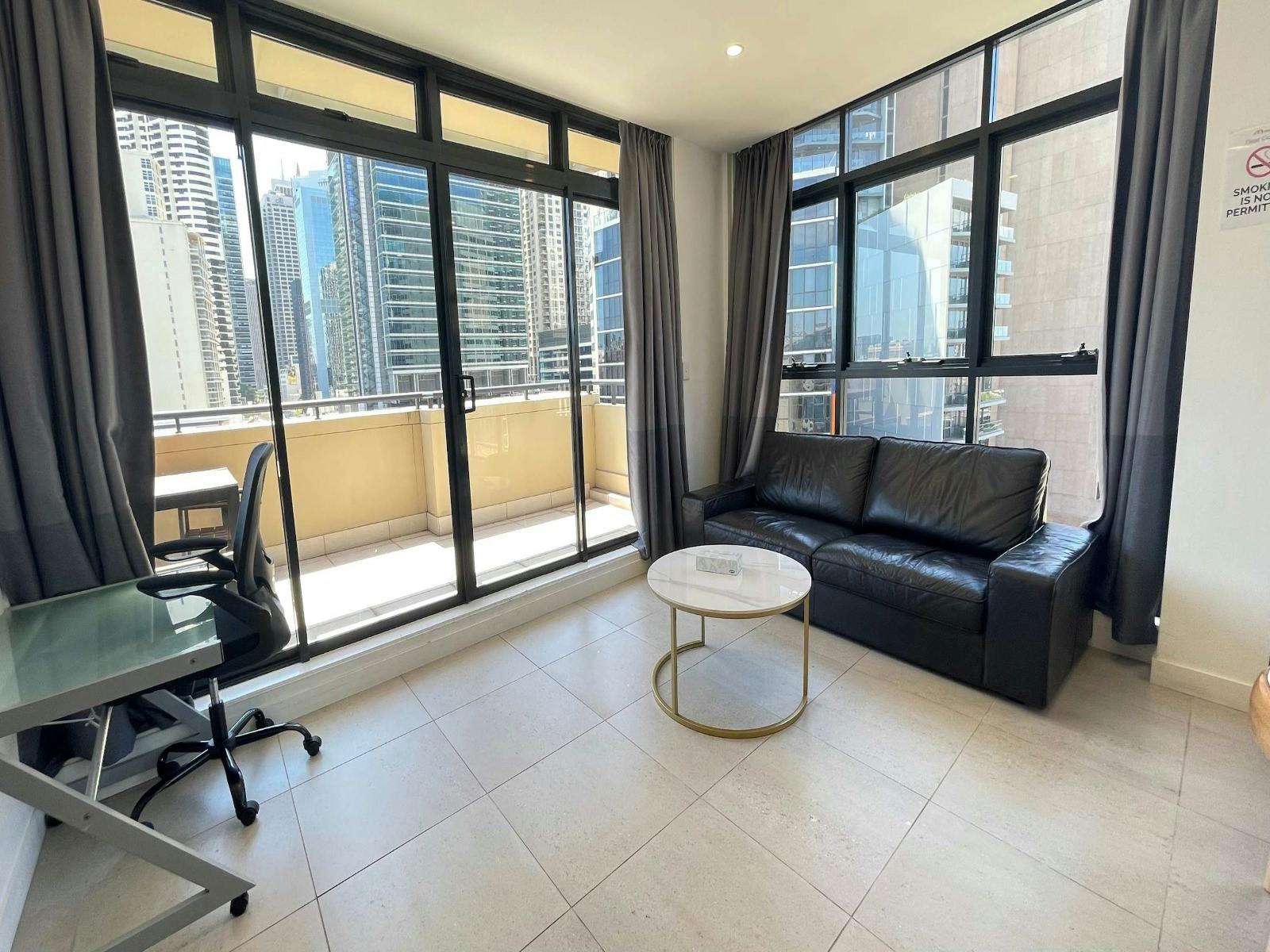 Living room with leather sofa, coffee table, and floor-to-ceiling windows.