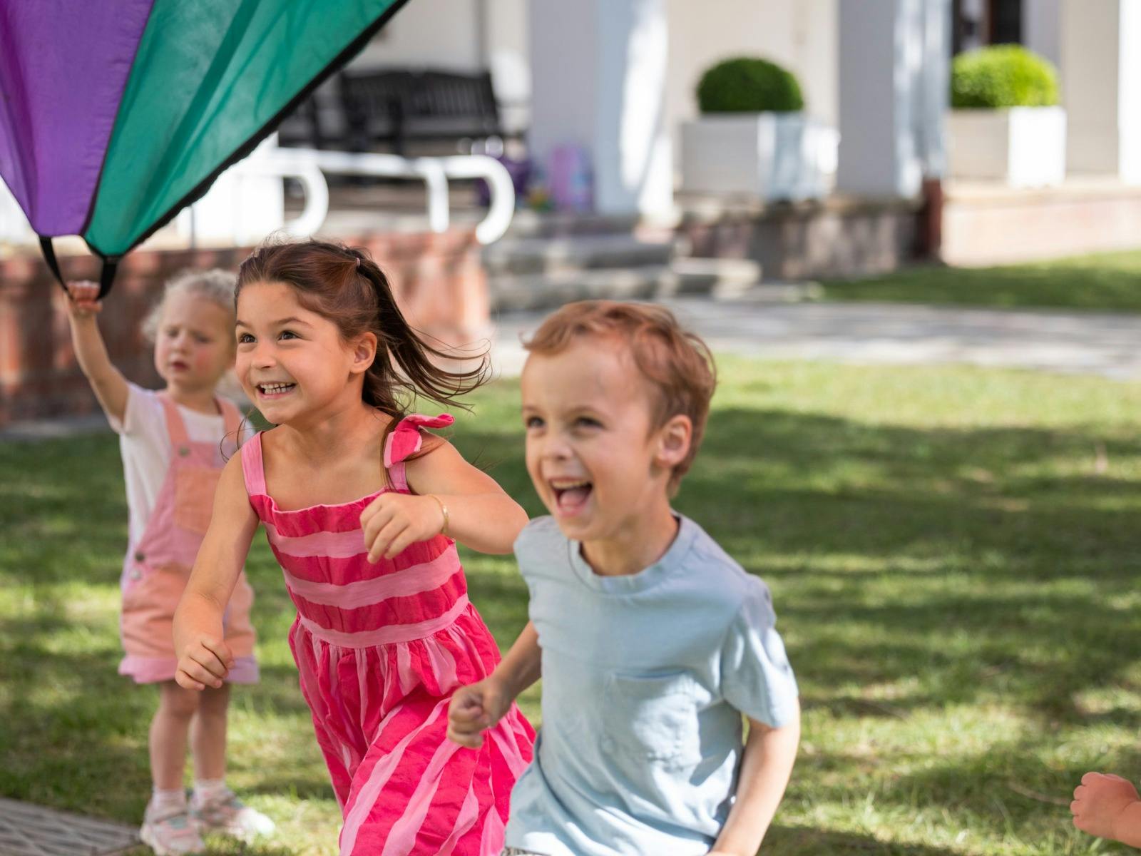A young girl and boy running beneath a parachute.