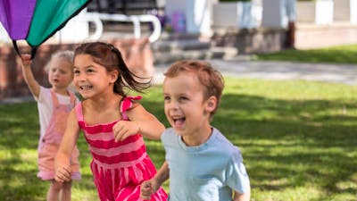 A young girl and boy running beneath a parachute.