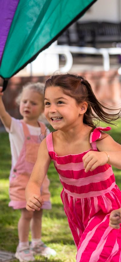 A young girl and boy running beneath a parachute.